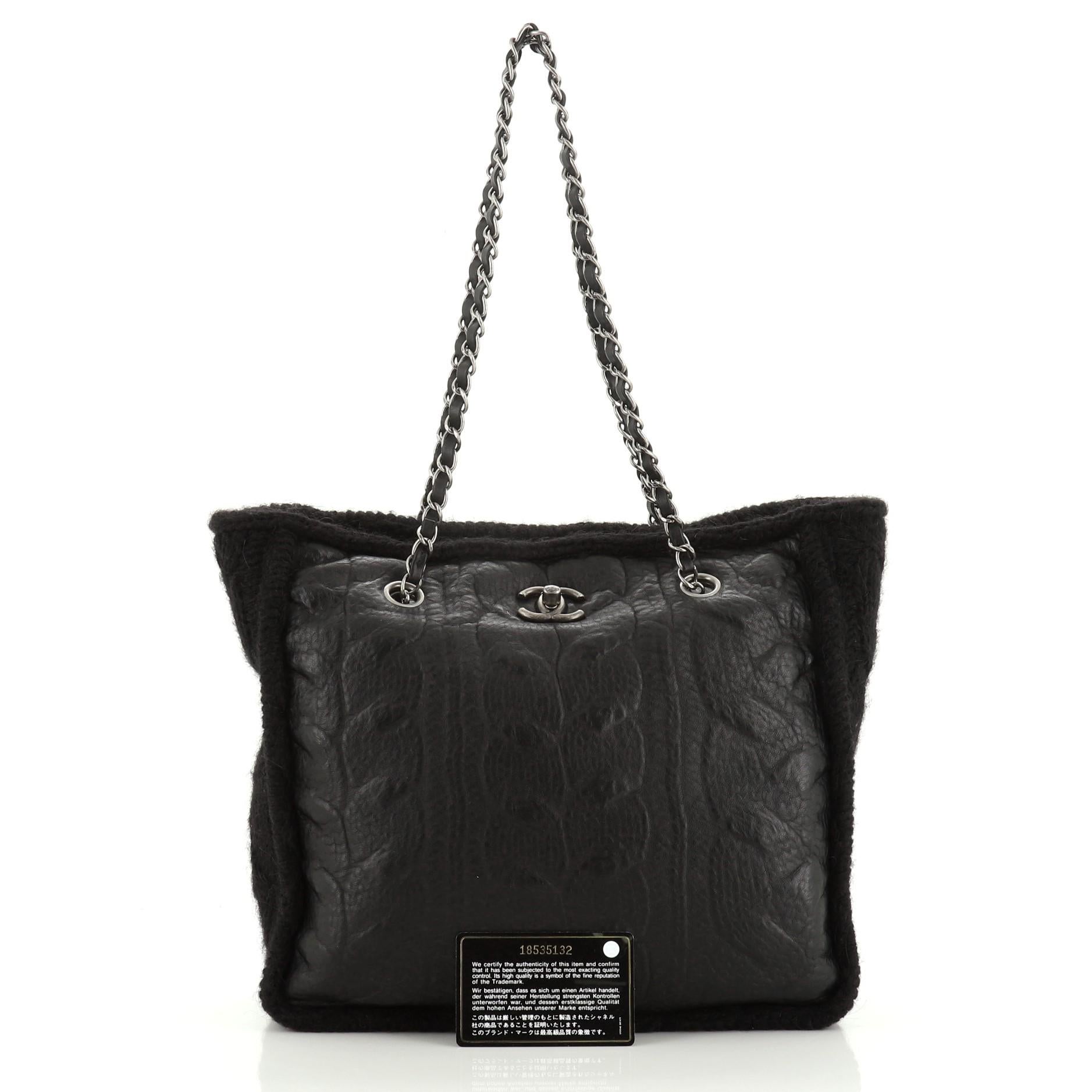 This Chanel Chic Knit Tote Sheepskin and Wool Medium, crafted from black wool and leather, features a woven in chain link strap, CC logo at the front, and aged silver tone hardware. Its closure opens to a black leather interior. Hologram sticker