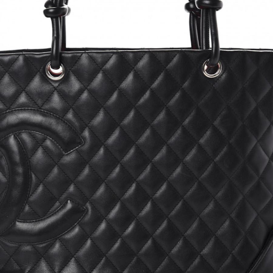 This tote is beautifully crafted of luxurious diamond quilted calfskin leather in black. The bag features a prominent black patent leather Chanel CC logo patch, rolled black leather strap handles with knotted ends, and silver hardware. The top