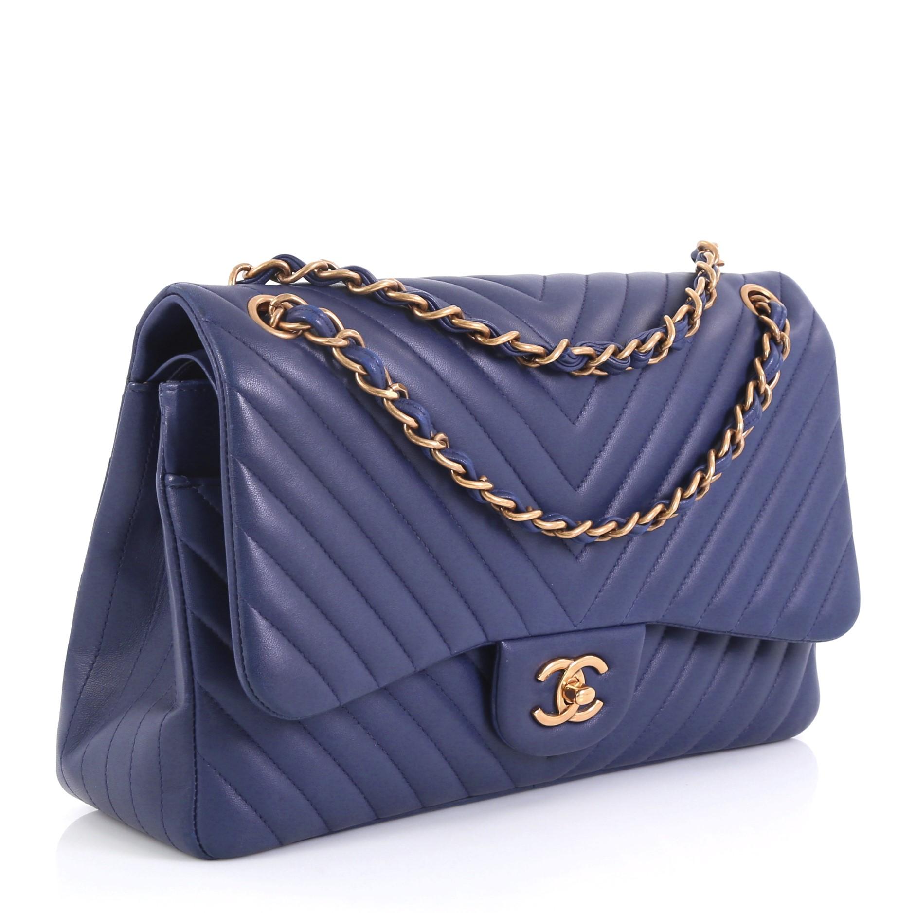 This Chanel Classic Double Flap Bag Chevron Lambskin Jumbo, crafted from blue chevron lambskin leather, features woven-in leather chain strap, exterior back slip pocket, and aged gold-tone hardware. Its double flap and CC turn-lock closure opens to