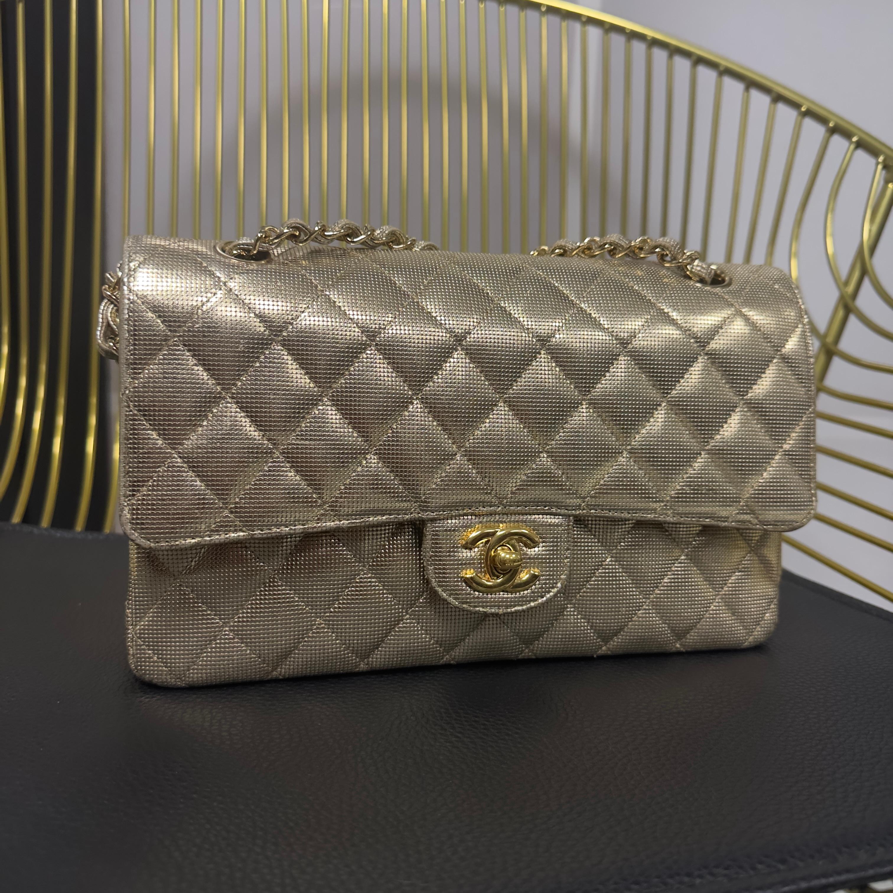 Una espléndida y rarísima Chanel Classic Flap 25 cm en piel metalizada caviar oro, una edición especial de la textura martelé luminosa. Esta versión combina el diseño icónico del trapuntato con un acabado metálico trabajado y brillante, ideal para