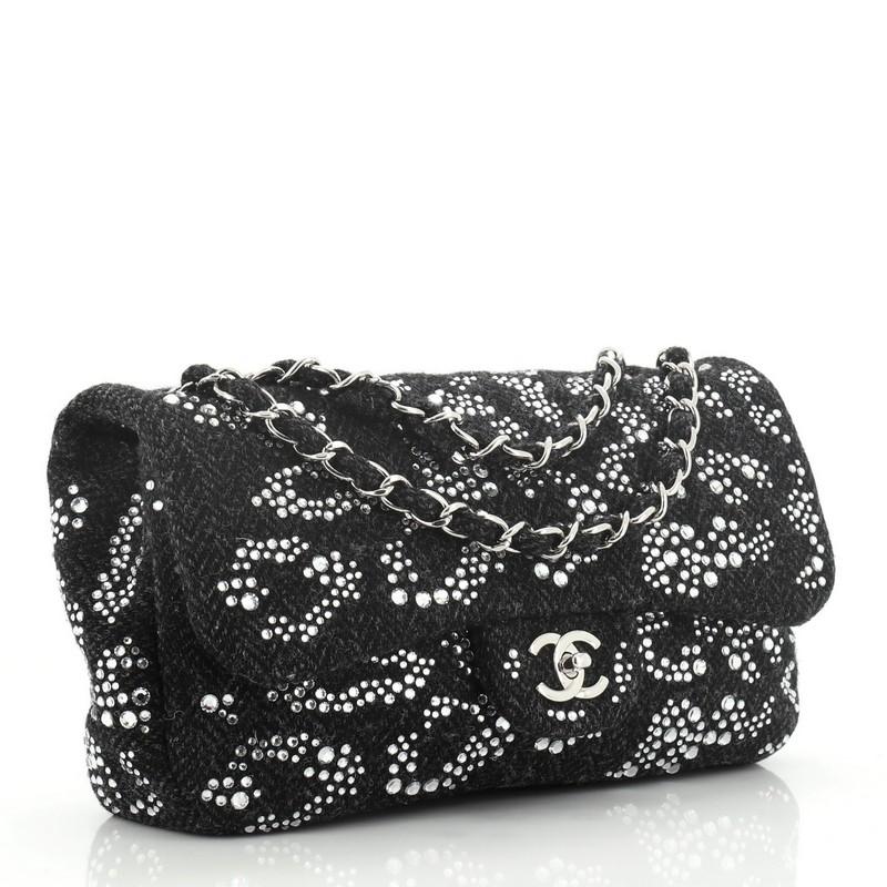 This Chanel Classic Flap Bag Strass Embellished Tweed Medium, crafted in black strass embellished tweed, features woven-in tweed chain-link strap, exterior back pocket, and silver-tone hardware. Its CC turn-lock closure opens to a black fabric