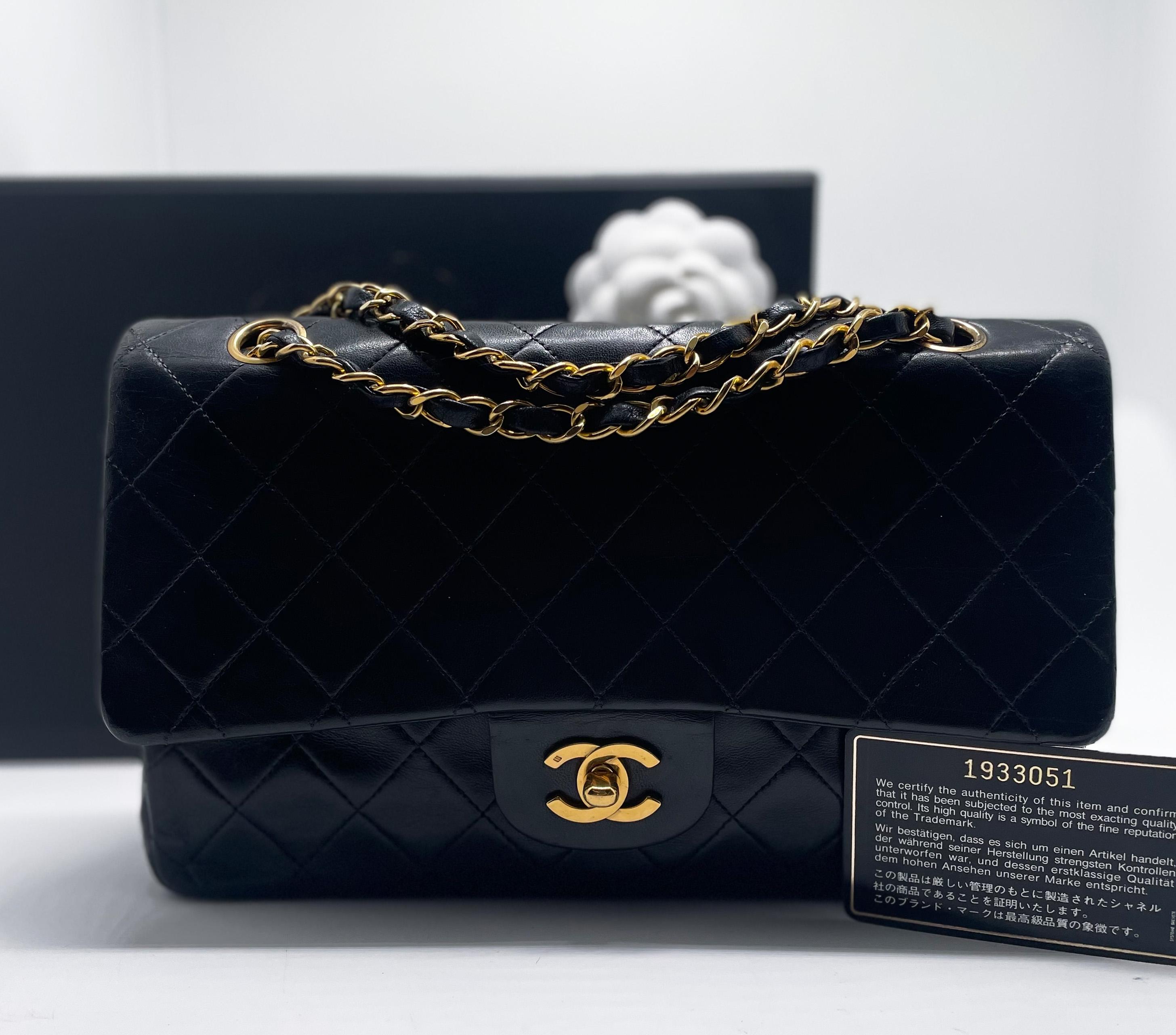 Indémodable sac à main Chanel Classique en cuir d'agneau noir et métal doré 24 carats. Ce must have est doté d'un double rabat Timeless en cuir matelassé noir, d'une chaîne en métal doré entrelacée de cuir noir qui permet de le porter à la main ou à