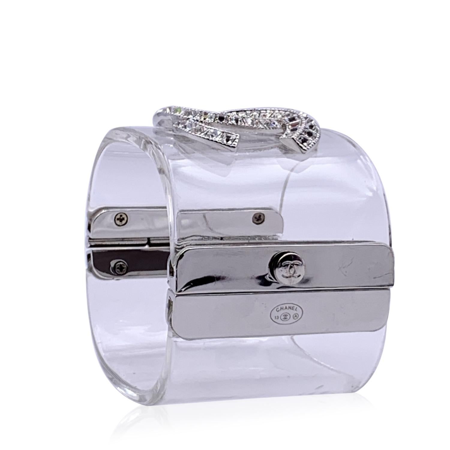 Lovely cuff bracelet by CHANEL. Clear resin with silver metal CC logo embellished with crystals at center. Slide lock closure. Stamped 'CHANEL 13 CC A' . Height: 2 inches - 5,1 cm. Will fit up to approx. 7 inches - 17.8 cm wrist.

Retail price is
