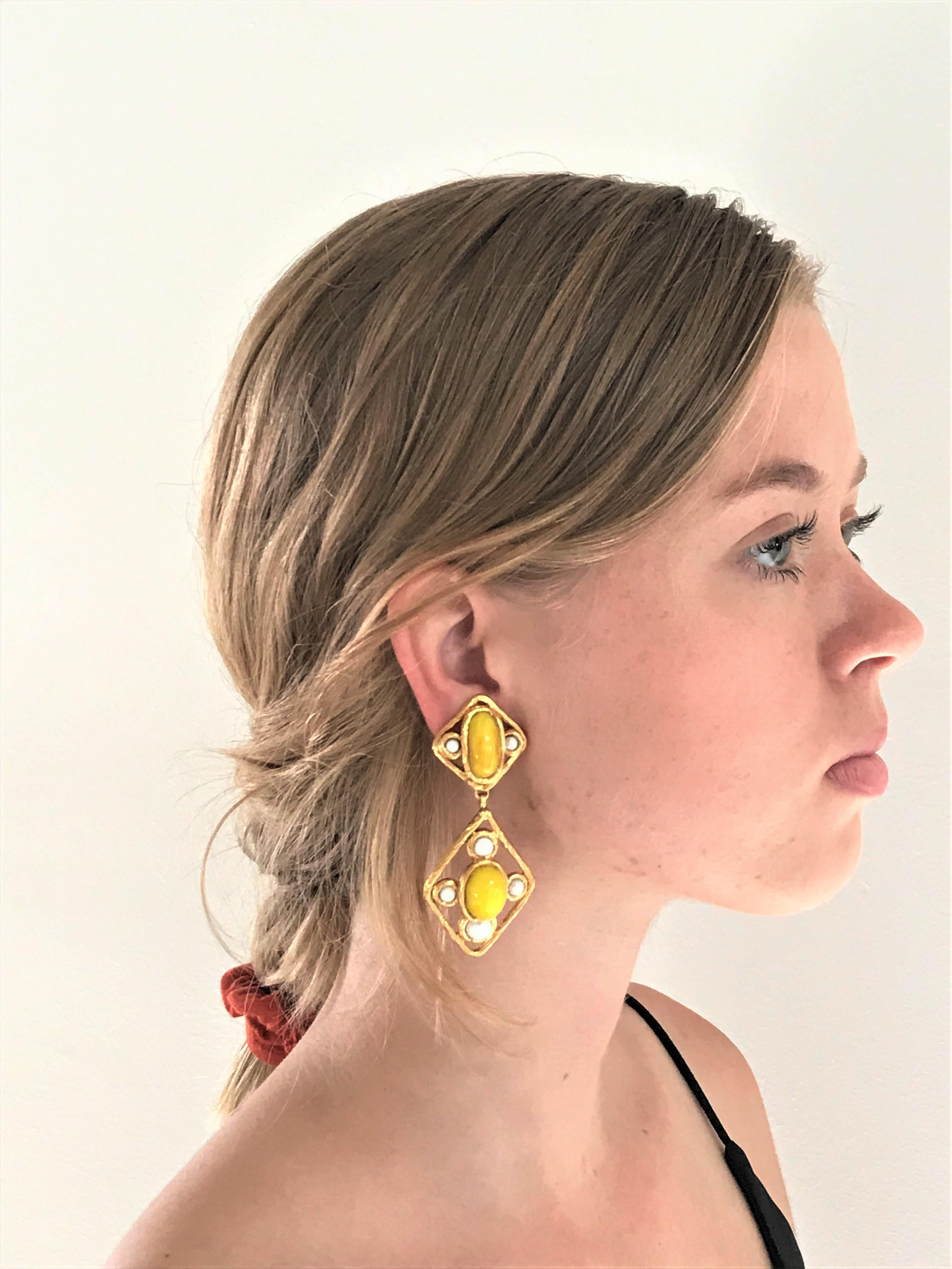 CHANEL Ohrclip (Made in France), 2 teilig mit trachenförmigem Anhänger mit gelber und weißer Glaspaste, vergoldet, um 2000, sehr guter Zustand.

Maße: 
Länge 7, 5 cm, obere Teil 2,6 x 2,6 cm, untere beweglicher  Drachen 4,4 x 3 cm 
Breite  3   
