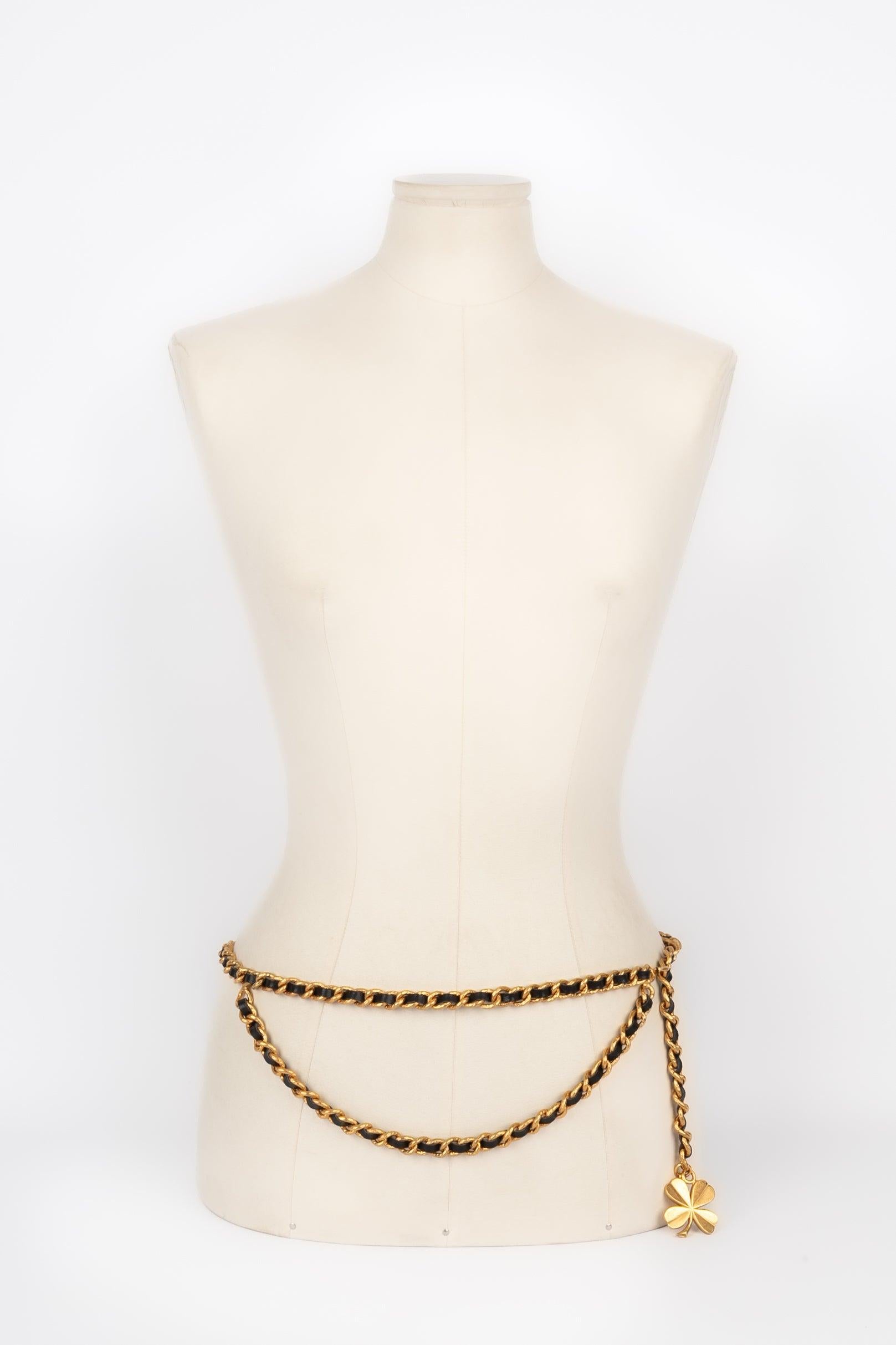 Chanel - (Made in France) Golden metal belt composed of a chain interlaced with black leather and holding a clover charm.
 
 Additional information: 
 Condition: Very good condition
 Dimensions: Length: 90 cm
 
 Seller Reference: CCB102