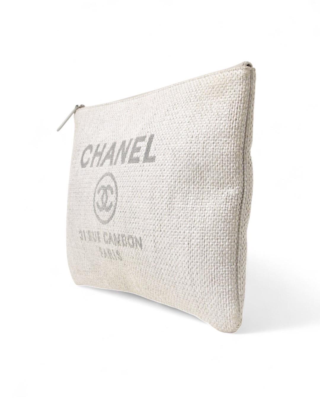 Pochette firmata Chanel, modello Deauville nella misura medium, realizzata in tessuto grigia con hardware argento. Dotata di una chiusura superiore a zip, internamente rivestita in nylon trapuntato tono su tono, la pochette è abbastanza capiente.