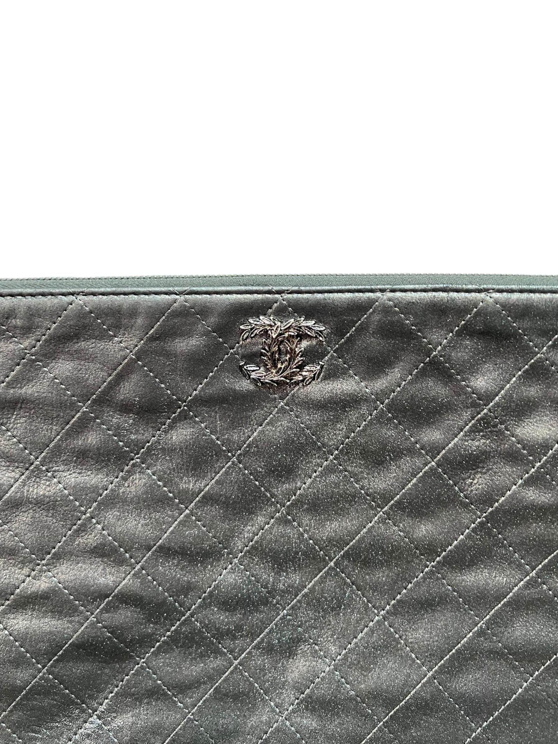 Clutch firmata Chanel, modello Flower, realizzata in pelle grigio satinato con hardware argentati. Dotata di una chiusura superiore a zip, internamente rivestita in tessuto grigio chiaro, capiente per l’essenziale. Presenta il classico logo “CC”