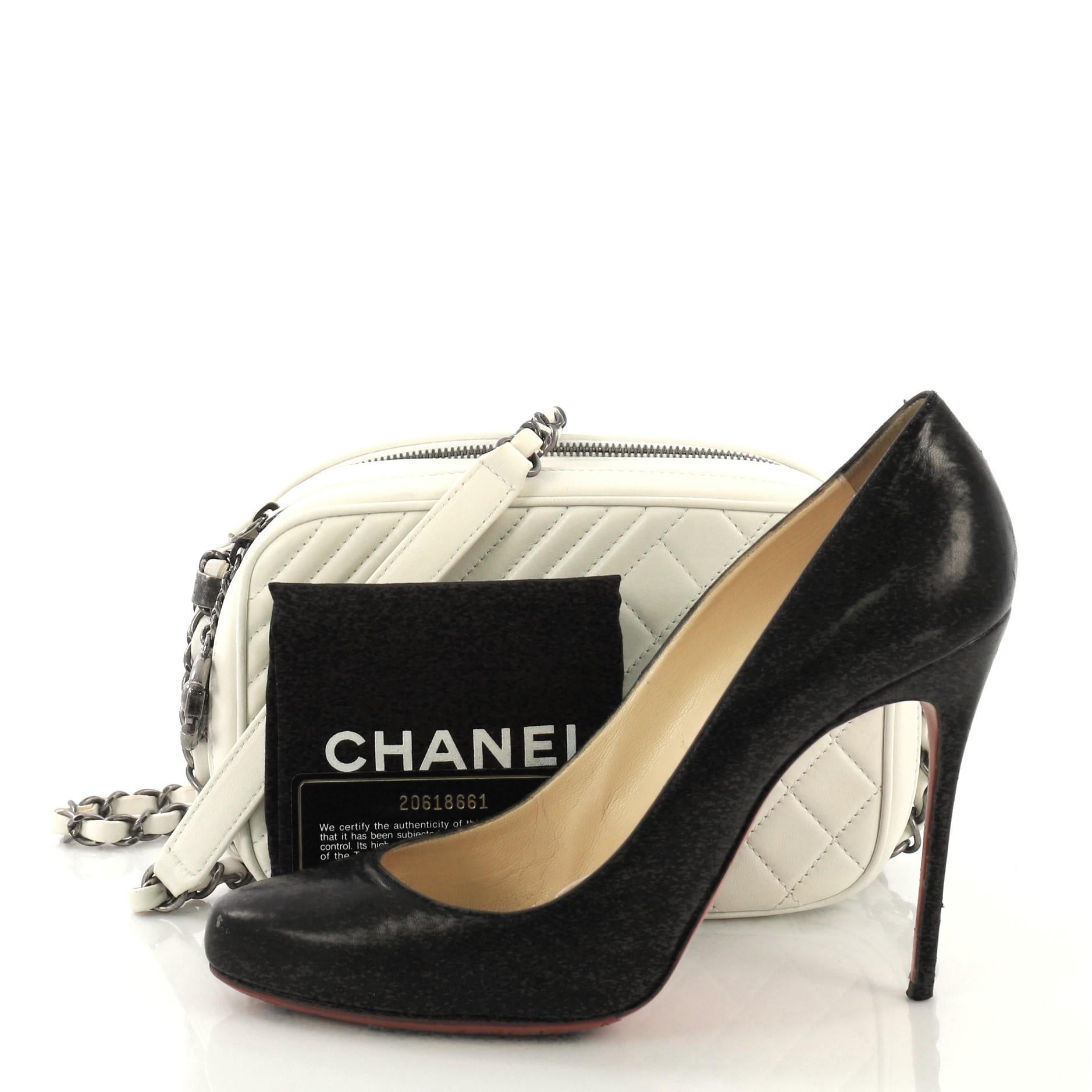 This Chanel Coco Boy Camera Bag Quilted Leather Small, crafted from white quilted leather, features woven-in leather chain link strap with leather pad, two zip compartments, oversized CC charm and aged silver-tone hardware. Its zip closures open to