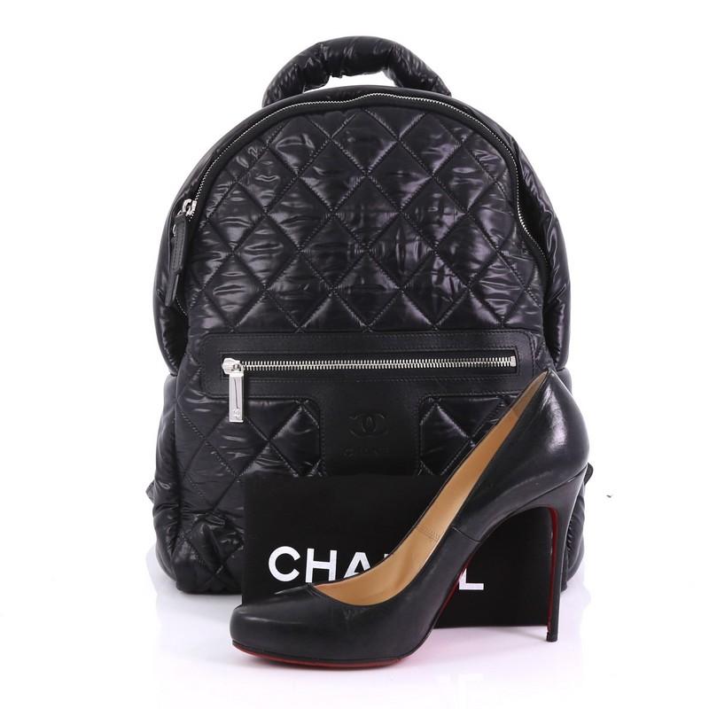 This Chanel Coco Cocoon Backpack Quilted Nylon Large, crafted from black quilted nylon, features a padded top handle, adjustable backpack straps, exterior front zip pocket, and silver-tone hardware. Its zip closure opens to a burgundy nylon interior