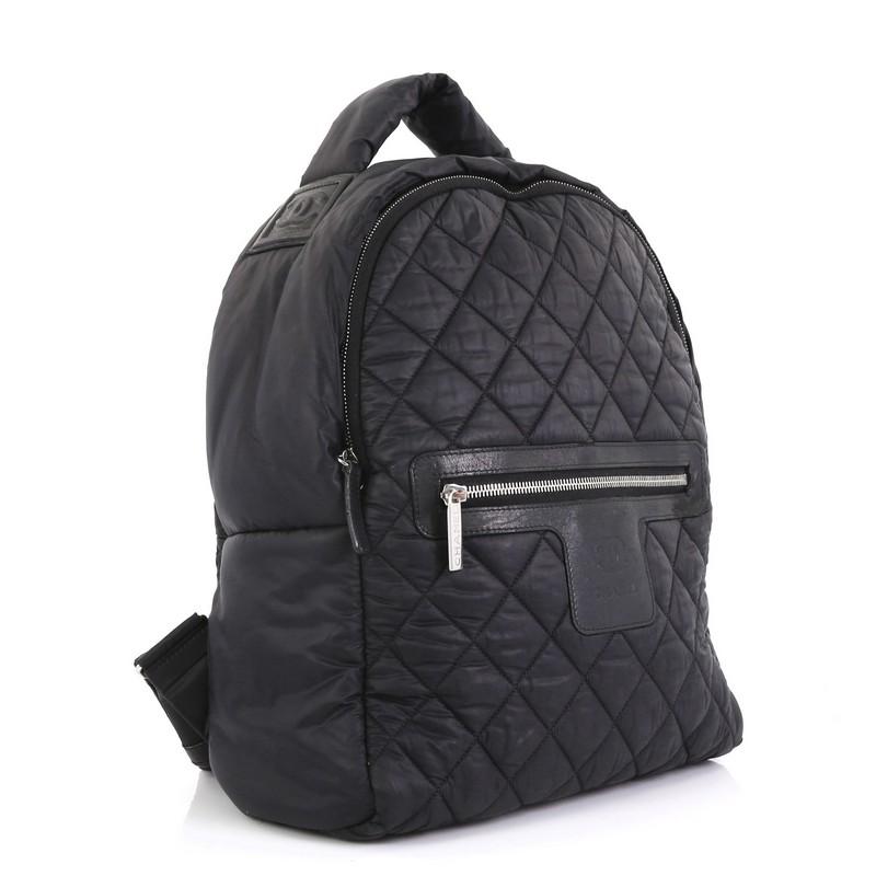 This Chanel Coco Cocoon Backpack Quilted Nylon Large, crafted from black quilted nylon, features a padded top handle, adjustable backpack straps, exterior front zip pocket, and silver-tone hardware. Its zip closure opens to a red nylon interior with