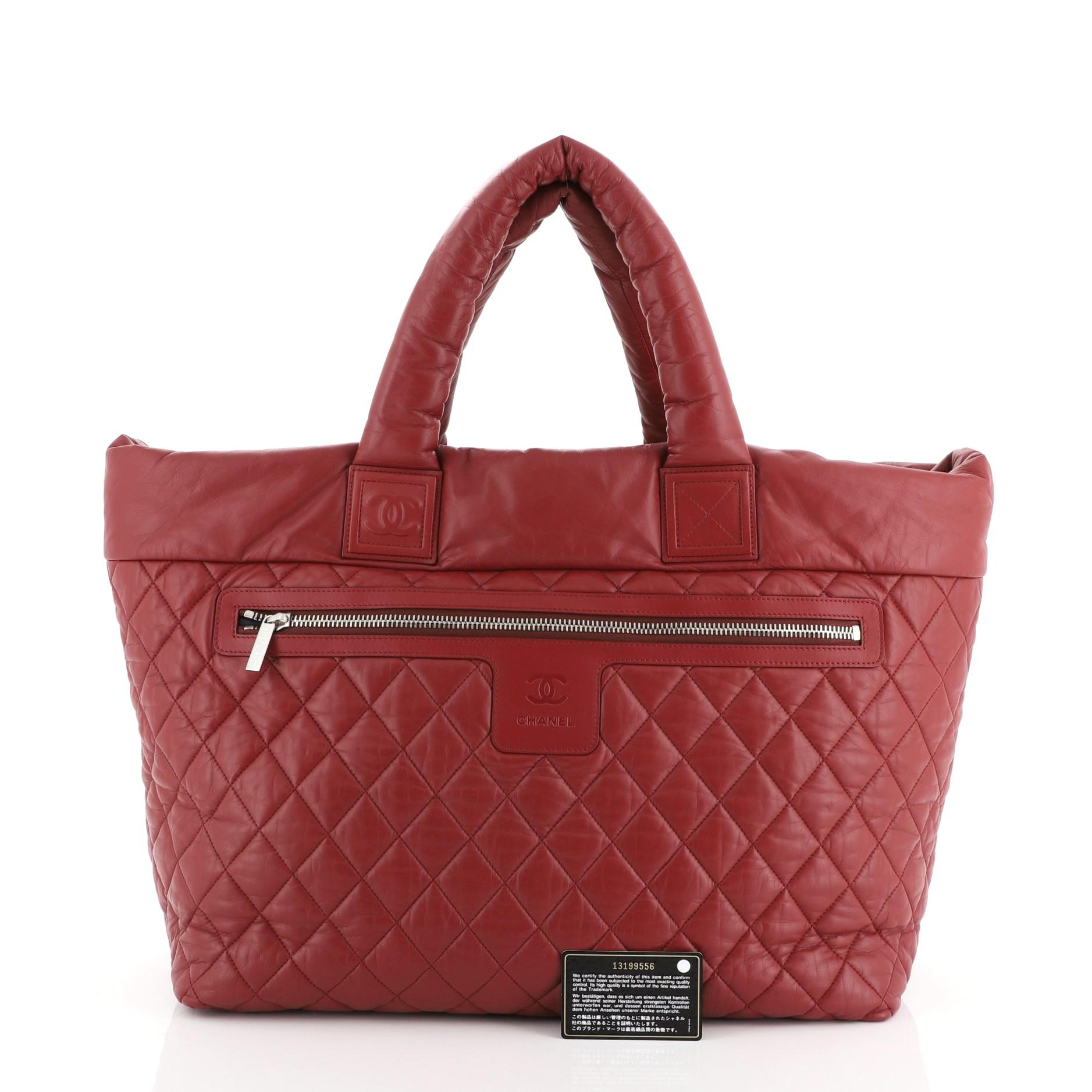 This Chanel Coco Cocoon Reversible Tote Quilted Lambskin Large, crafted from red lambskin leather, this sporty-chic tote features dual padded top handles, interlocking CC logo design, leather trims and silver-tone hardware accents. Its clasp closure