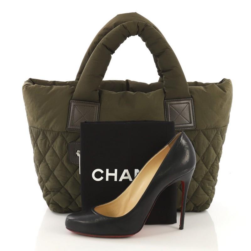 This Chanel Coco Cocoon Reversible Tote Quilted Nylon Small, crafted from green quilted nylon, features padded top handles, exterior zip pocket, and silver-tone hardware. Its clasp band closure opens to a reversible red nylon interior with zip