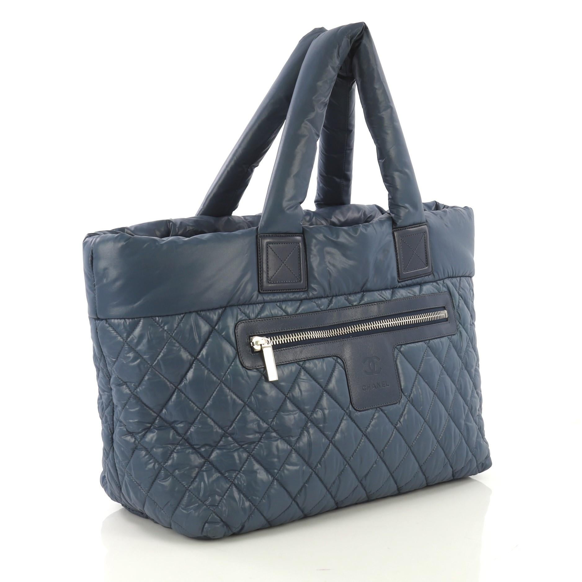 This Chanel Coco Cocoon Zipped Tote Quilted Nylon Large, crafted from blue quilted nylon, features padded top handles, exterior zip pocket, and silver-tone hardware. Its zip closure opens to a black nylon interior with zip pocket. Hologram sticker