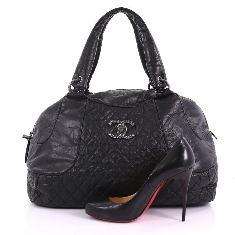 This Chanel Coco Rider Bowler Bag Quilted Aged Calfskin Large, crafted from black quilted aged calfskin leather, features dual top handles, protective base studs, and aged silver-tone hardware. Its zip closure opens to a dark red fabric interior