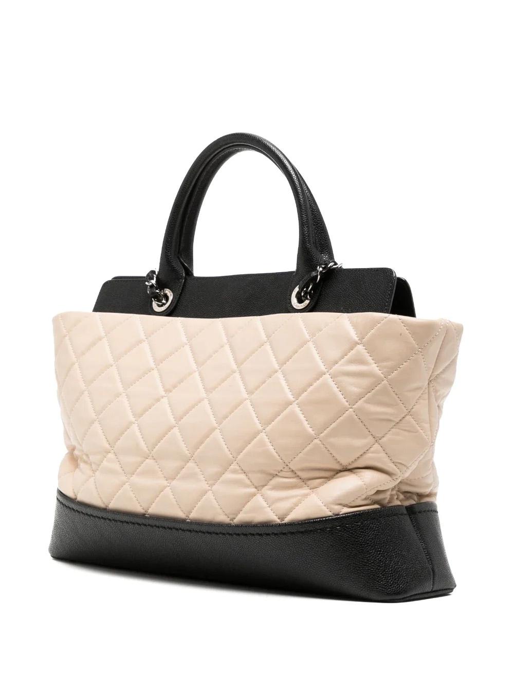 This Coco Shopping Tote is crafted from a combination of beige lambskin and black caviar leather. It features diamond quilting, a logo charm and two rolled top handles. Further, it offers two leather and chain-link shoulder straps and a signature