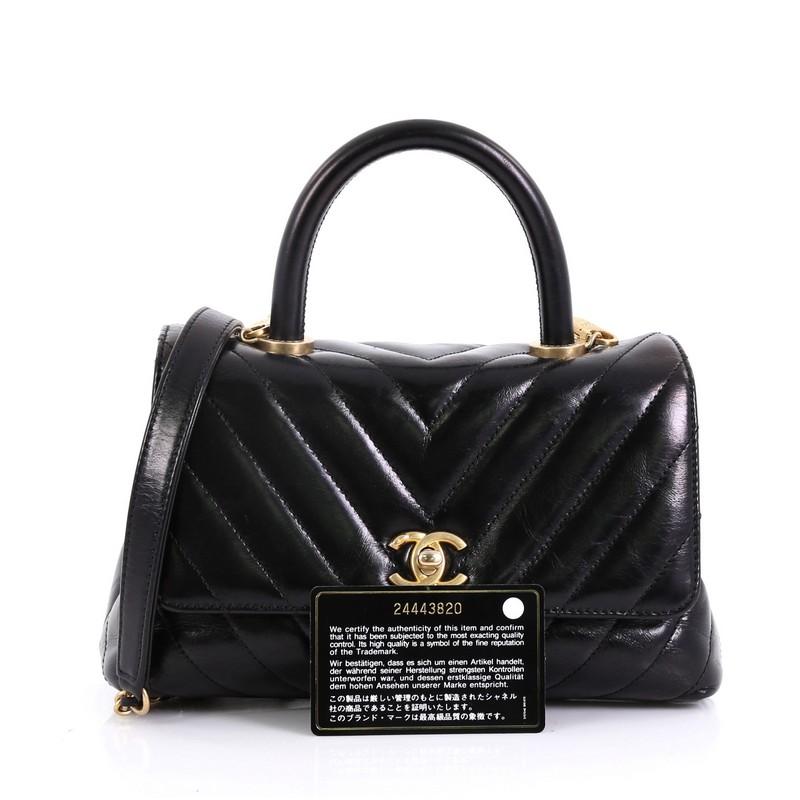 This Chanel Coco Top Handle Bag Chevron Calfskin Mini, crafted in black chevron calfskin, features a single loop leather handle and matte gold-tone hardware. Its CC turn-lock closure opens to red fabric interior with a middle slip compartment and