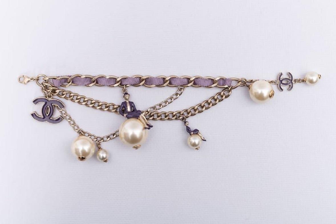 Chanel (Made in France) Light gilted metal chain bracelet entwined with purple fabric and adorned with false pearls and enamelled charms. 
Spring-Summer 2004 collection. 
Signed on a plate.

Additional information:

Dimensions: 
Length: 18 cm (7.09