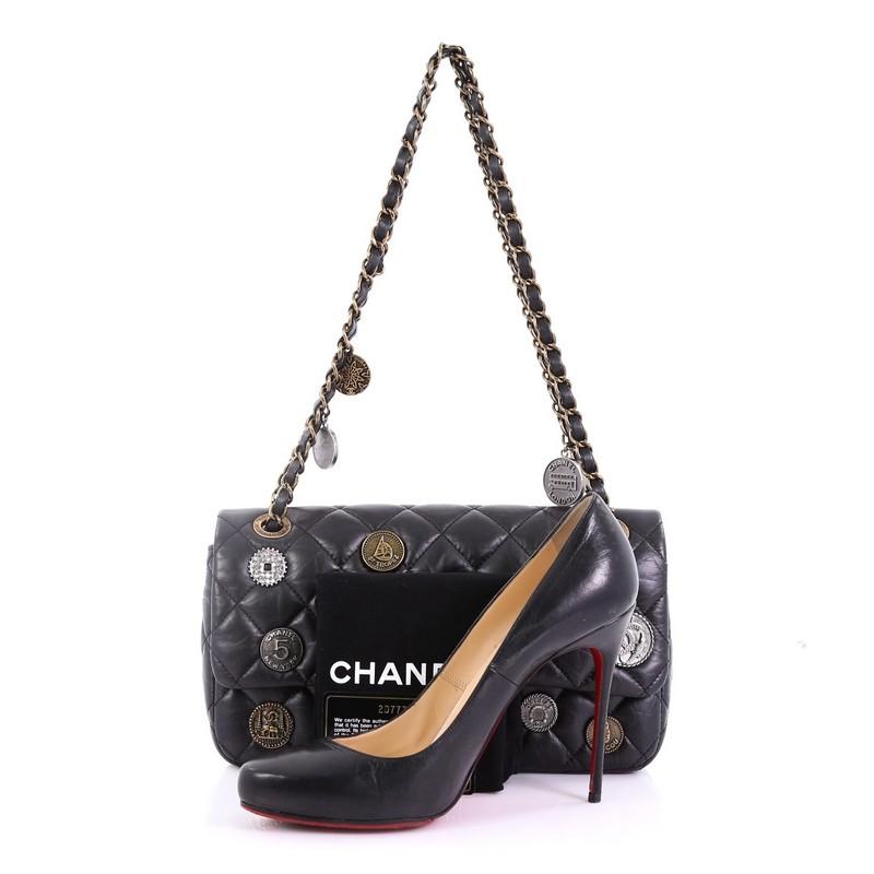 This Chanel Coin Medallion Flap Bag Quilted Aged Calfskin Medium, crafted from black quilted aged calfskin leather, features woven-in leather chain straps, engraved Chanel logo coins, exterior back pocket, and aged gold-tone hardware. Its CC