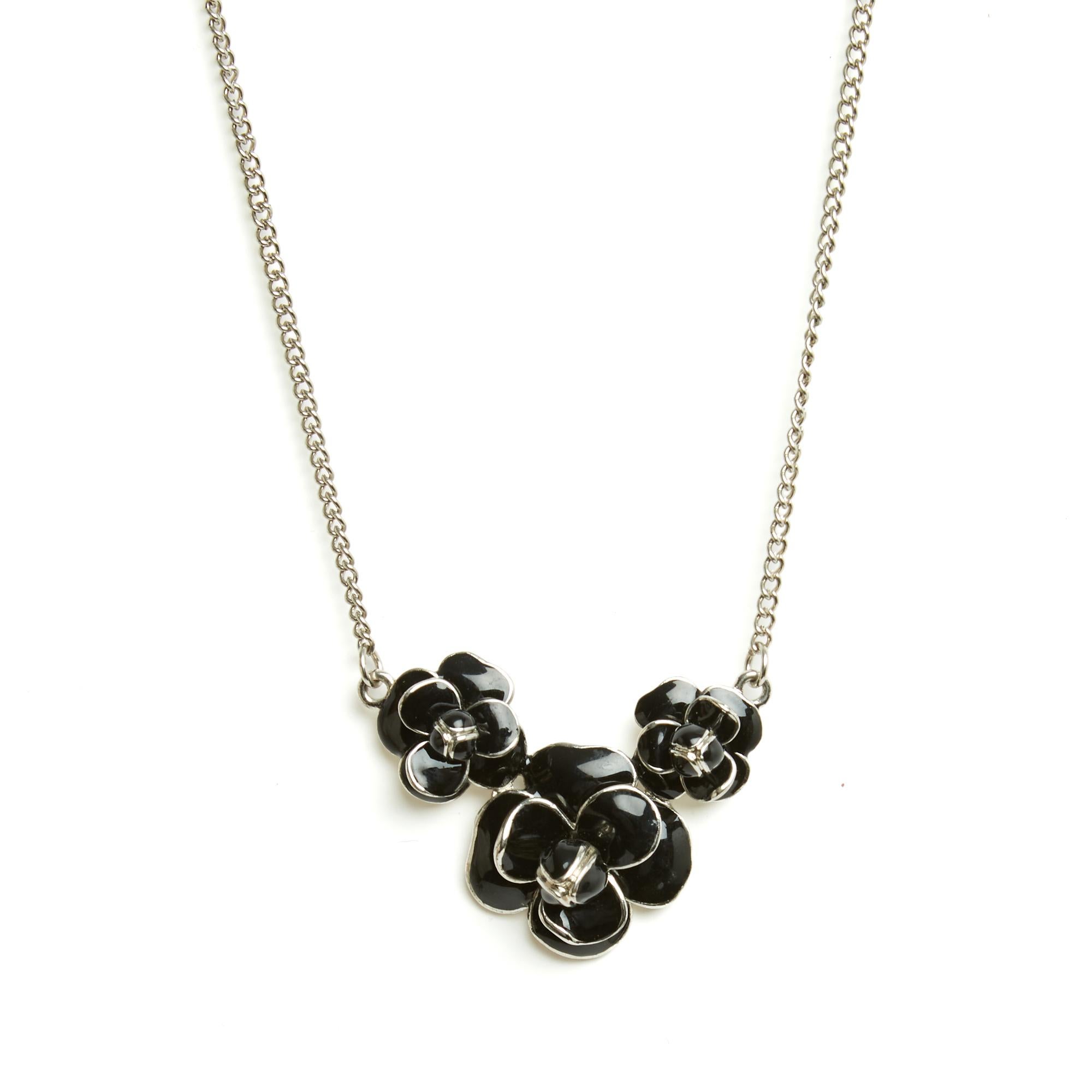 A Chanel necklace circa 2011 in silver-tone metal, composed of a curb chain and a large central pendant featuring three camellias covered in black enamel. The necklace fastens with a lobster clasp on a ring extended by a chain, and bears the small