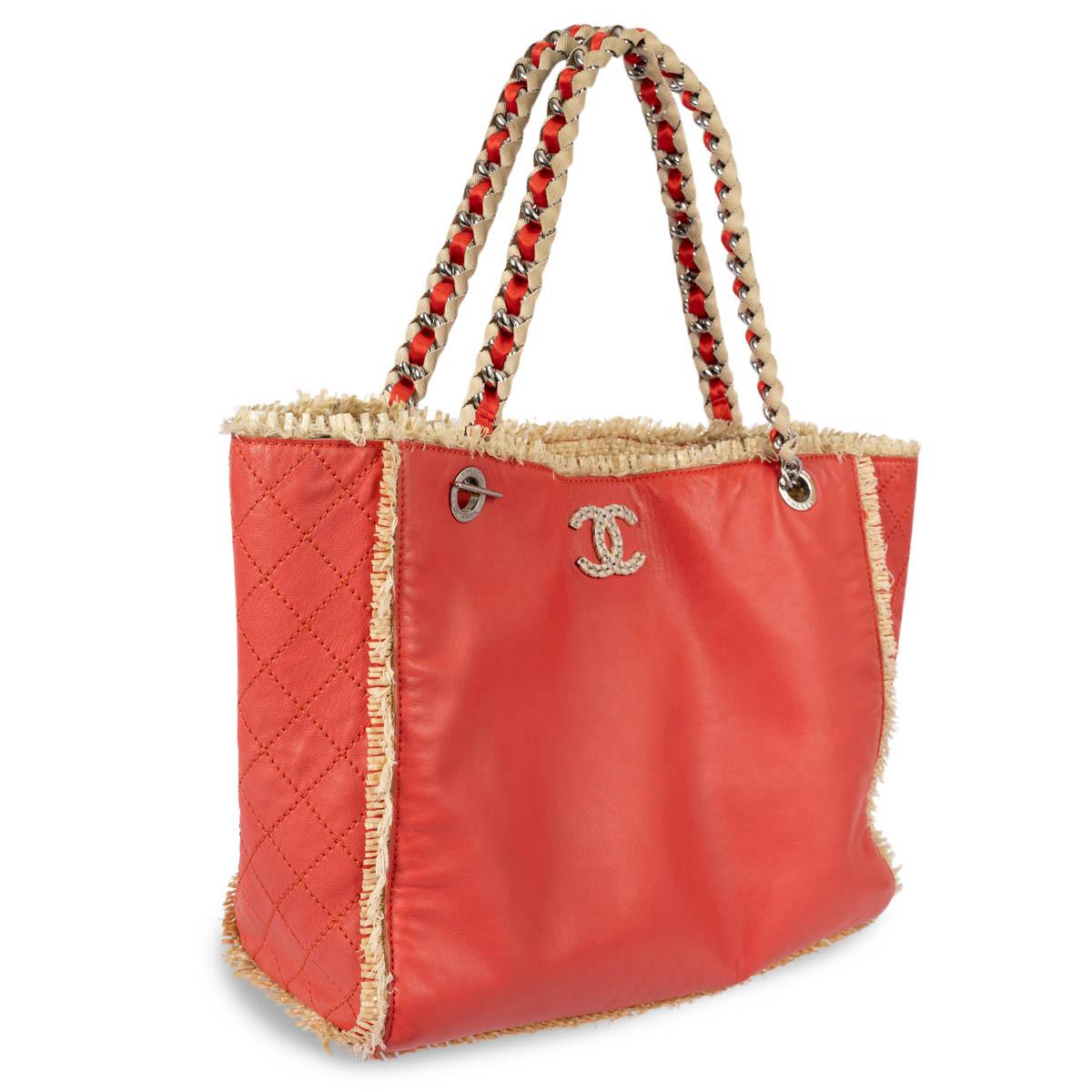 100% authentic Chanel Tweedy shopping tote in smooth coral leather with beige raffia fringed hem, quilted gussets on the side and red satin, beige grosgrain chain-link handles. Opens with a magnetic button on top and is lined in beige raffia with a