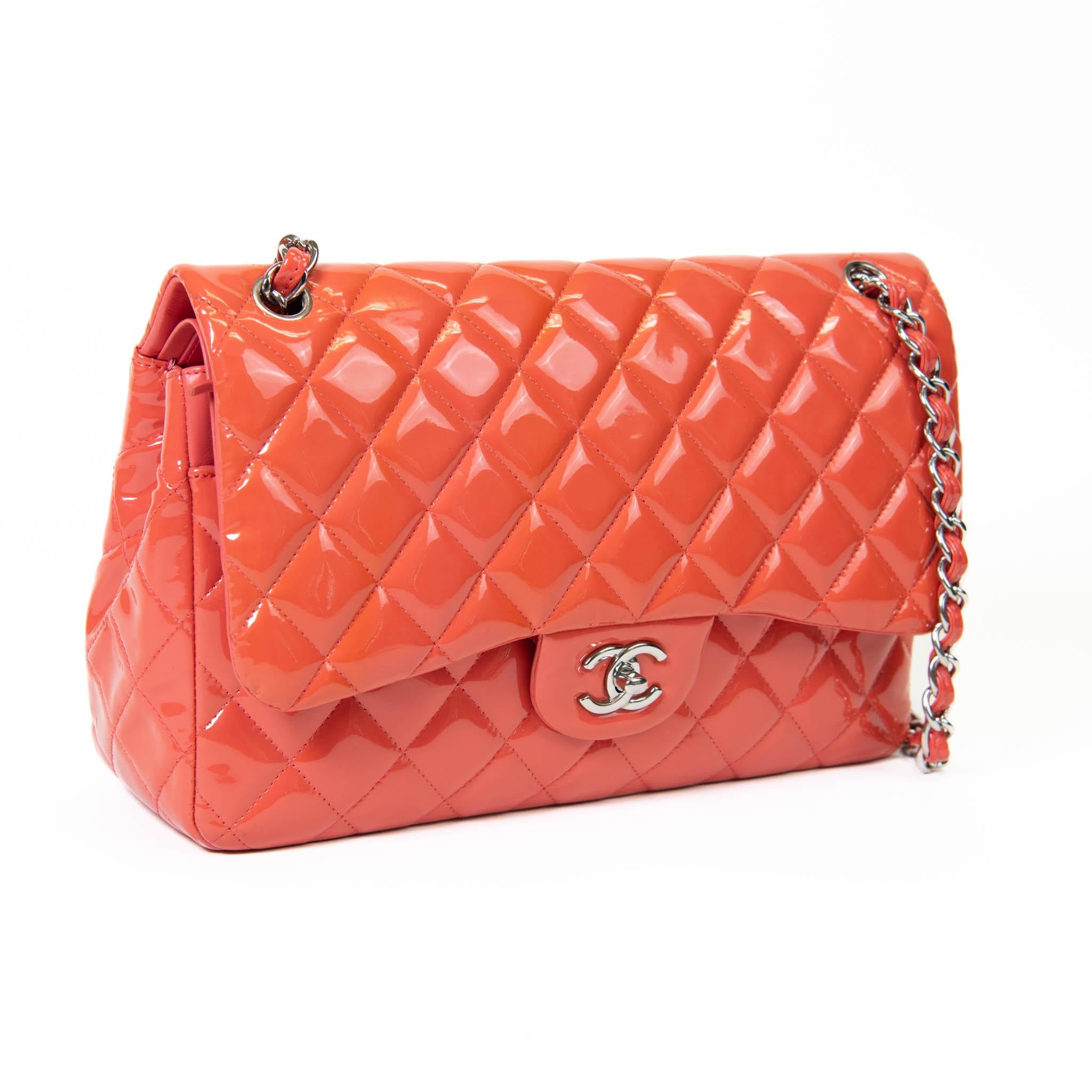 100% Authentic 

This shoulder bag showcases a classic Chanel double flap with luxurious diamond quilted patent leather in orange. The bag features a silver chain patent leather shoulder strap and a rear pocket. The front opens with a silver Chanel
