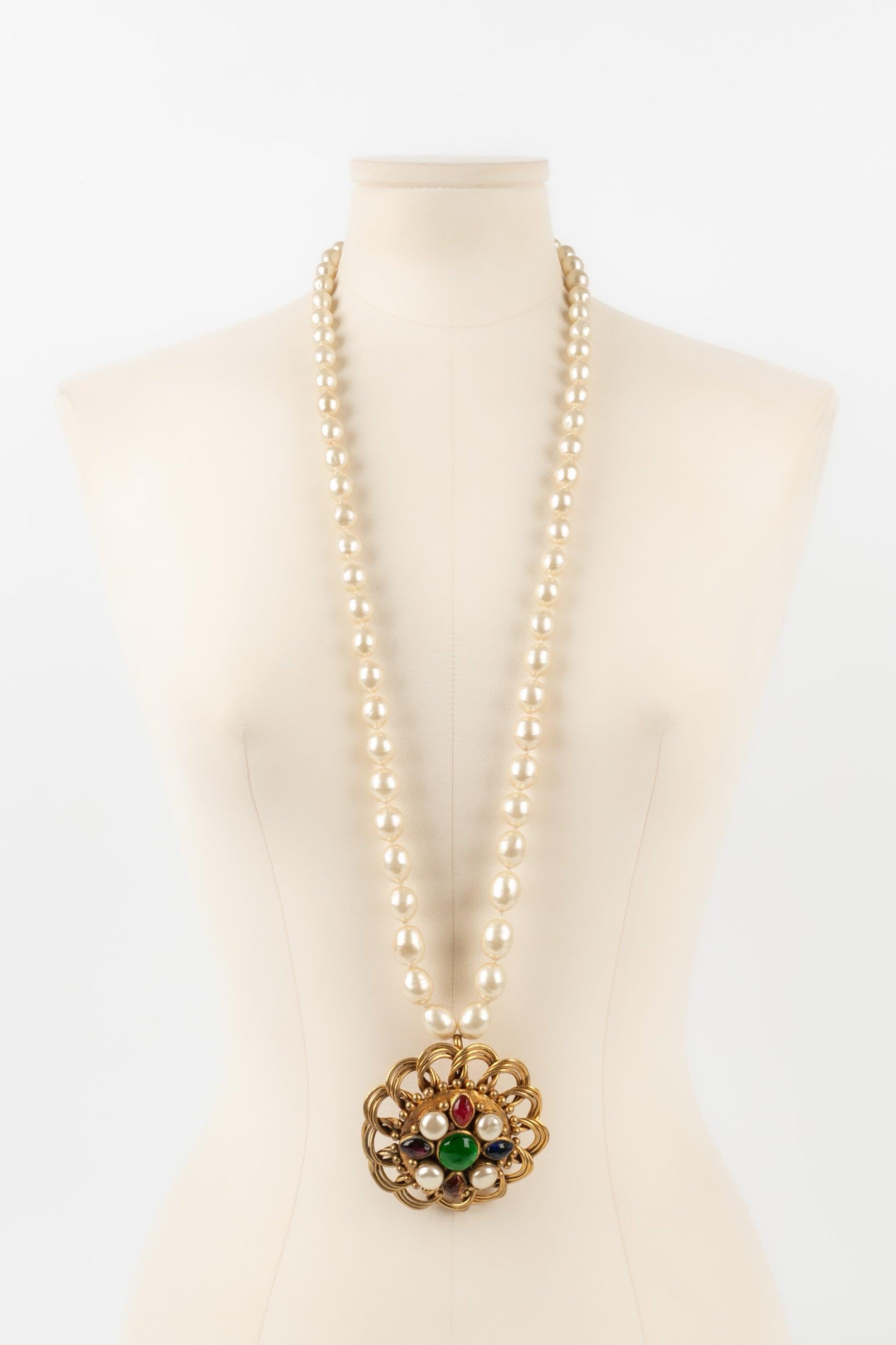 Chanel - (Made in France) Costume pearl necklace with a golden metal pendant ornamented with glass paste cabochons. 1984 Collection.

Additional information:
Condition: Good condition
Dimensions: Necklace length: 93 cm - Pendant diameter: 7.5