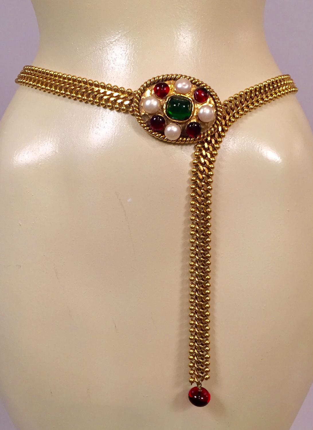 This statement making Chanel Couture belt is from the wardrobe of a former Chanel fashion executive. It is a gold chain belt with an oval belt buckle set with a large Gripoix green cabochon stone at the center. This is surrounded with four ruby red