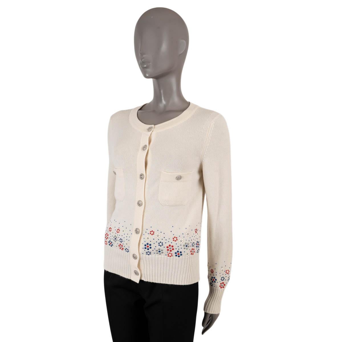 100% authentic Chanel round-neck cream cashmere (100%) cardigan embellished with red, grey, blue and cream floral studs and blue crystals. The design features two buttoned chest pockets, ribbed cuff and waistband and silver-tone CC logo front