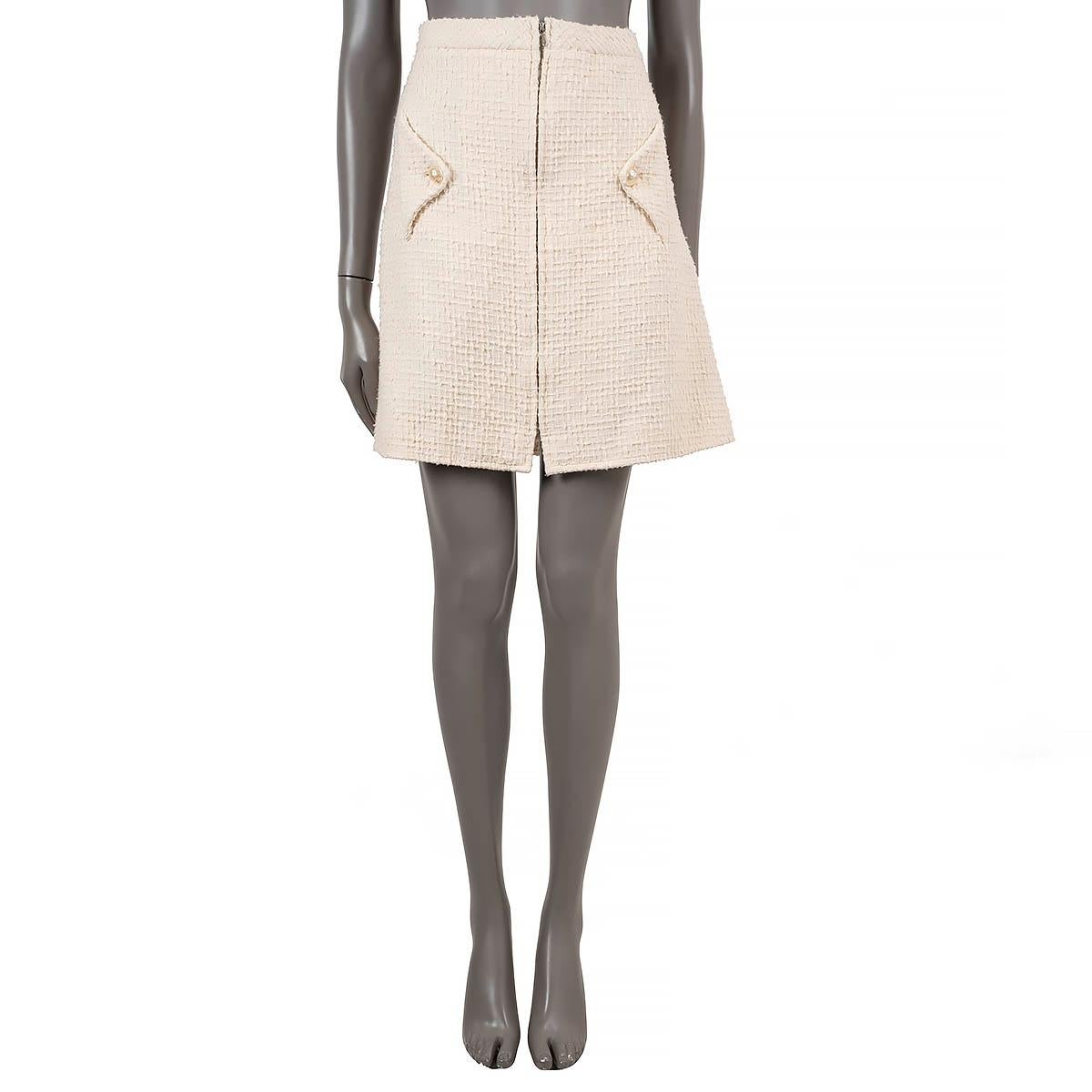 100% authentischer Chanel-Rock aus strukturiertem Tweed in cremefarbener Baumwolle (100%). Mit ausgestellter, knielanger Silhouette und zwei Pattentaschen mit Kunstperlenknöpfen an der Taille. Öffnet sich mit einem verdeckten Reißverschluss auf der