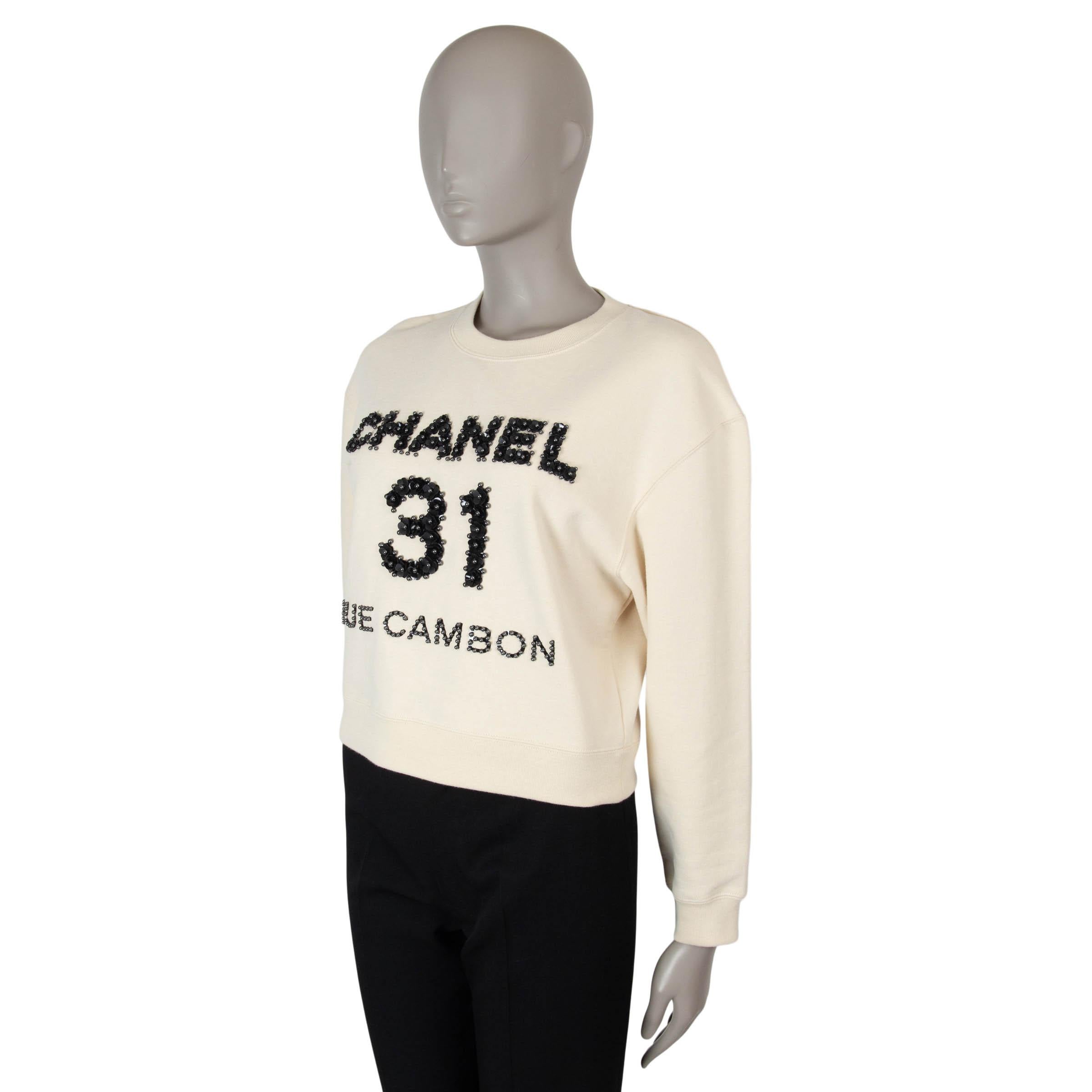 This 100% authentic Chanel sweatshirt in cream cotton jersey (100%) is adorned with black leather sequins and pearls for an elevated take on casualwear. Featuring a slightly cropped, boxy silhouette with dropped shoulders, it is finished with a