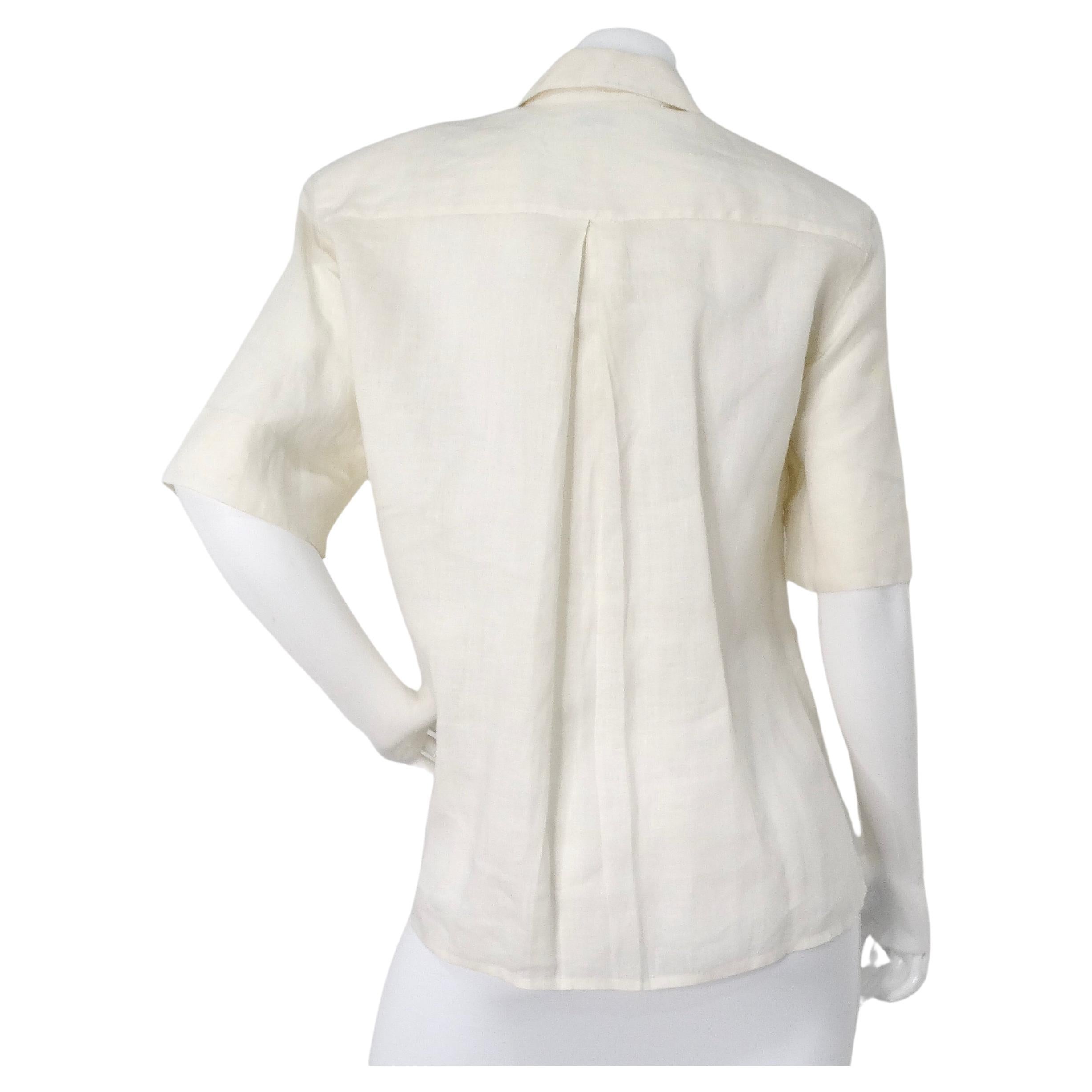 La camicetta a maniche corte Chanel Cream Linen Interlocking CC Button-Up degli anni '80 incarna un'eleganza senza tempo e un abbigliamento casual sofisticato. Realizzato in tessuto di lino bianco/crema, questo pezzo vintage emana uno stile chic