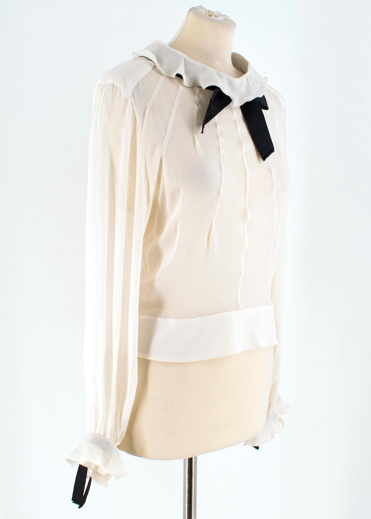 Chanel Cream Silk-Chiffon Blouse 

- Cream Silk-chiffon blouse
- Black bow detail at collar and sleeve
- Ruffled collar and cuffs
- Faux pearl detail 
- Quilted thin shoulder pads
- Seam paneling down front and back  
- Button fastening behind neck,