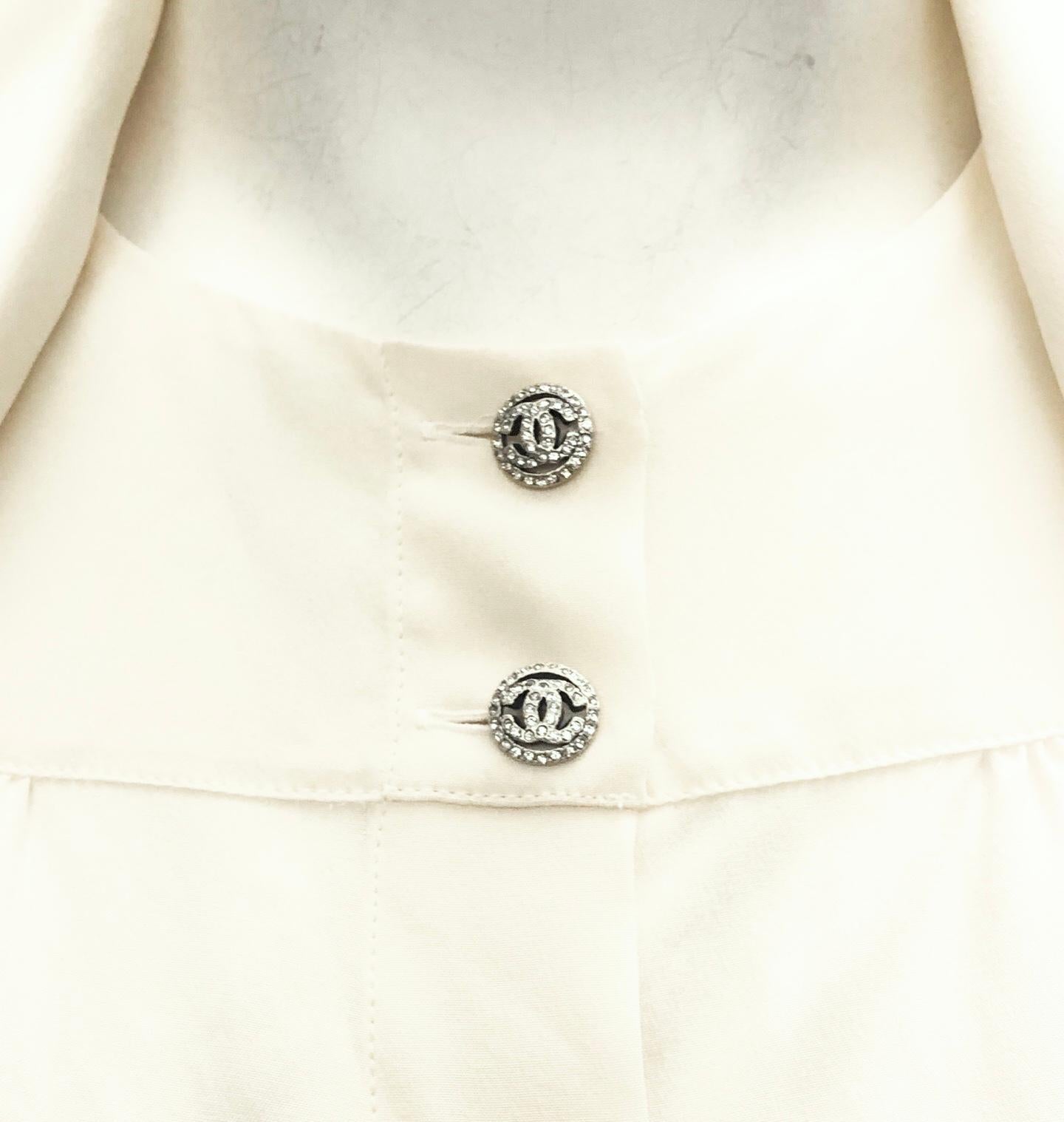 - Chanel cream silk cut out sleeve blouse from Fall year 2007 collection. 

- Gathered seams at shoulders, back and front. 

- Cut outs at sleeves creating a draped effect. 

-  Two silver tone crystal embellished CC buttons at collar and tonal tie