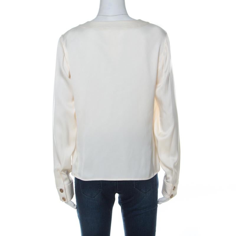 This blouse from Chanel features a minimal silhouette made from luscious silk fabric carrying an understated cream hue. It comes with full sleeves and a round neckline. Decorated with gold-tone engraved buttons on the front, this blouse makes for an