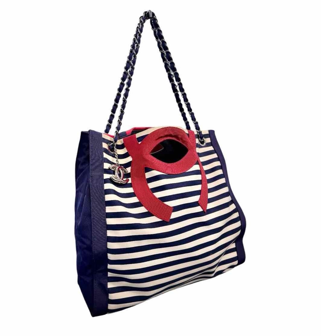 This classic tote bag is made of striped canvas and has an application of abstract linear patterns that are exciting and bold. The bag features a navy blue chain link canvas threaded shoulder straps and a hanging Chanel CC charm. This opens to a