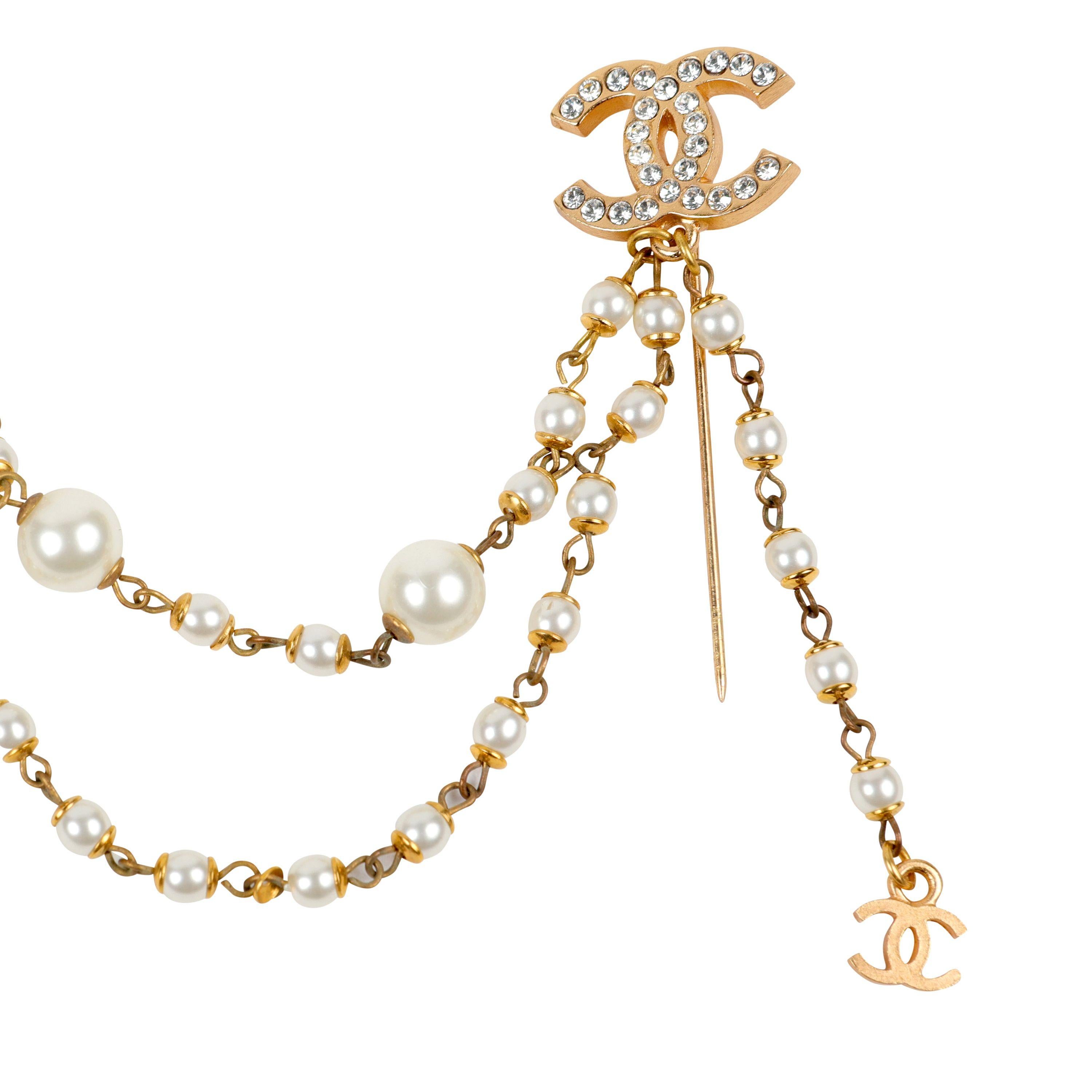 This authentic Chanel Crystal and Pearl Draped Chain Pin is pristine. Crystal adorned gold toned interlocking CCs are connected with draping pearl chains.  Made in France. Pouch or box included. 
PBF 13796
