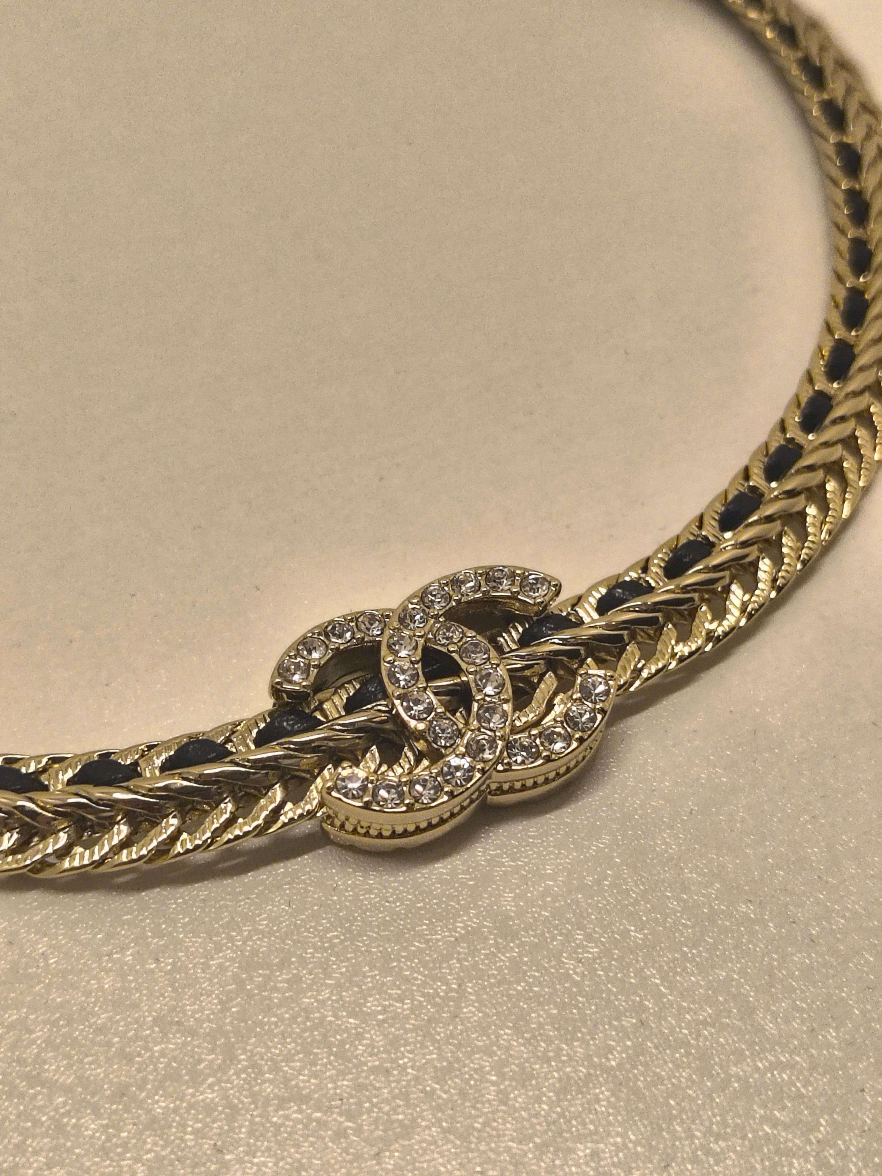 Questo girocollo Chanel è caratterizzato da una morbida pelle nera intrecciata a una catena dorata, impreziosita da file di cristalli scintillanti per una finitura glamour. Al centro, l'iconico logo CC a incastro è completamente incrostato di