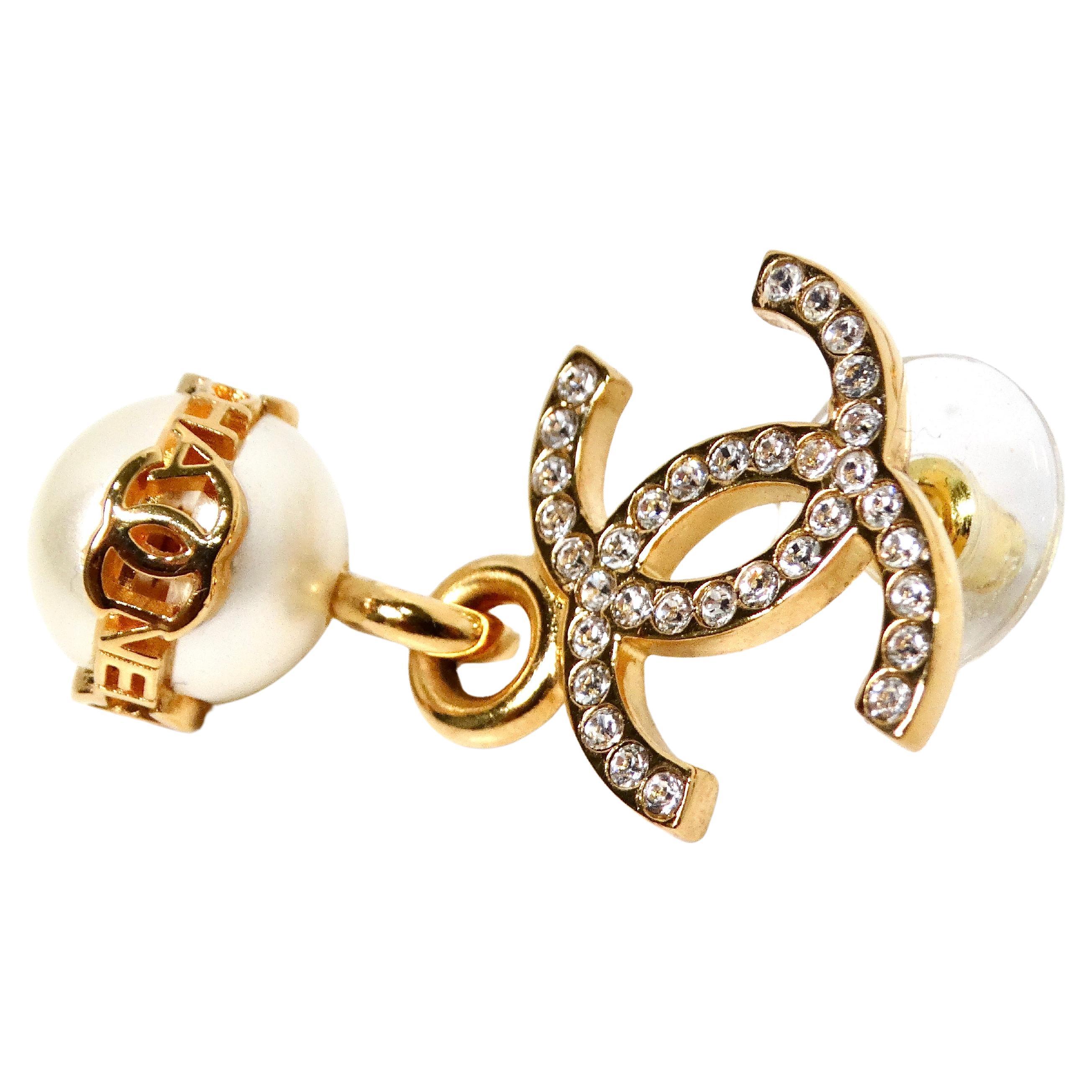 The Chanel Crystal Interlocking CC Costume Pearl Dangle Earrings for 2023 are a stunning embodiment of timeless elegance and contemporary sophistication. Crafted with meticulous attention to detail, these earrings feature a luminous faux pearl
