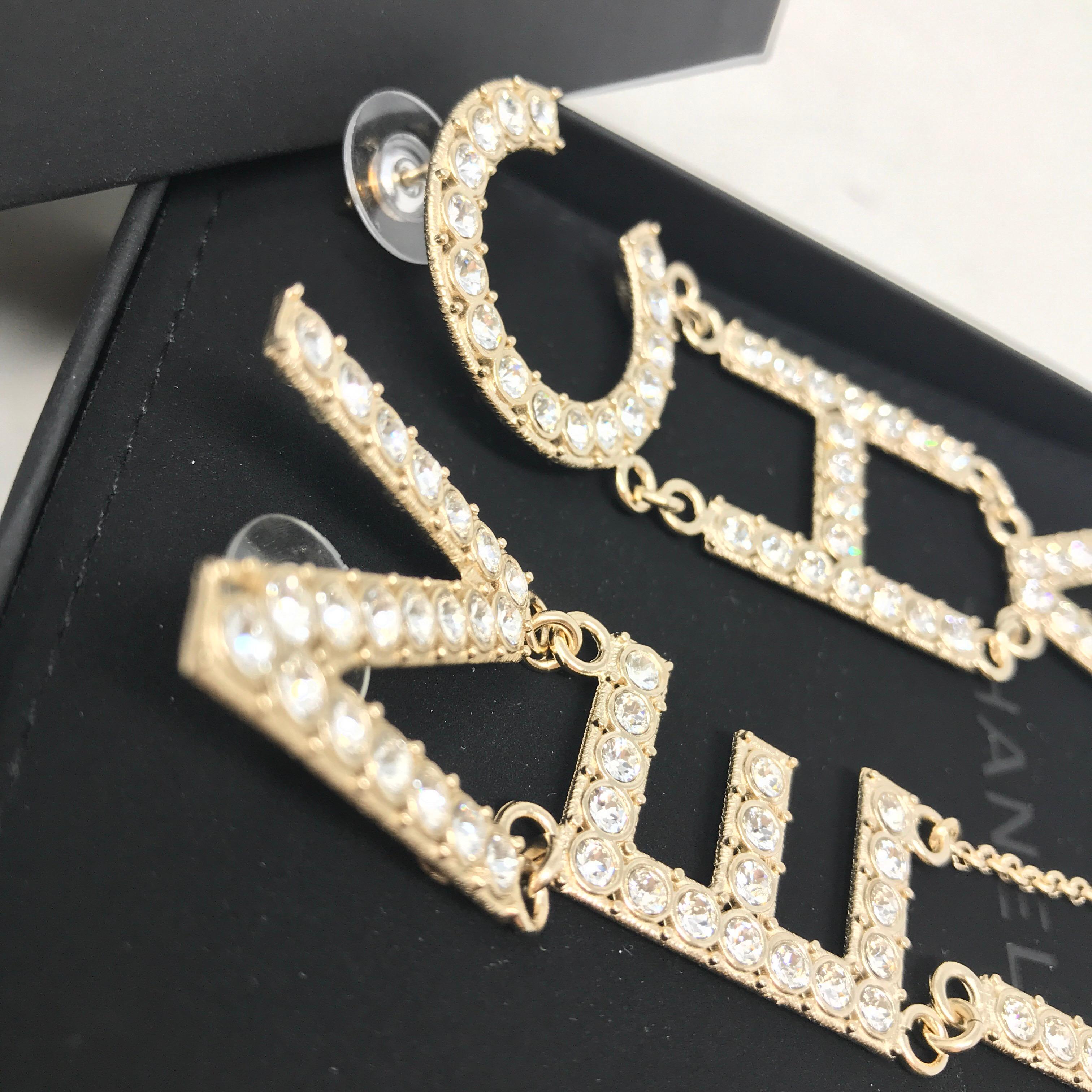 CHANEL Crystal Letter Logo Statement Dangle Earrings. Never used. Iconic runway design. “CHA” and “NEL” letter logo. Light gold tone with silver crystals. Dangle style for pierced ears. Approximately 9.6cm in length. Made in Italy. Comes with velvet