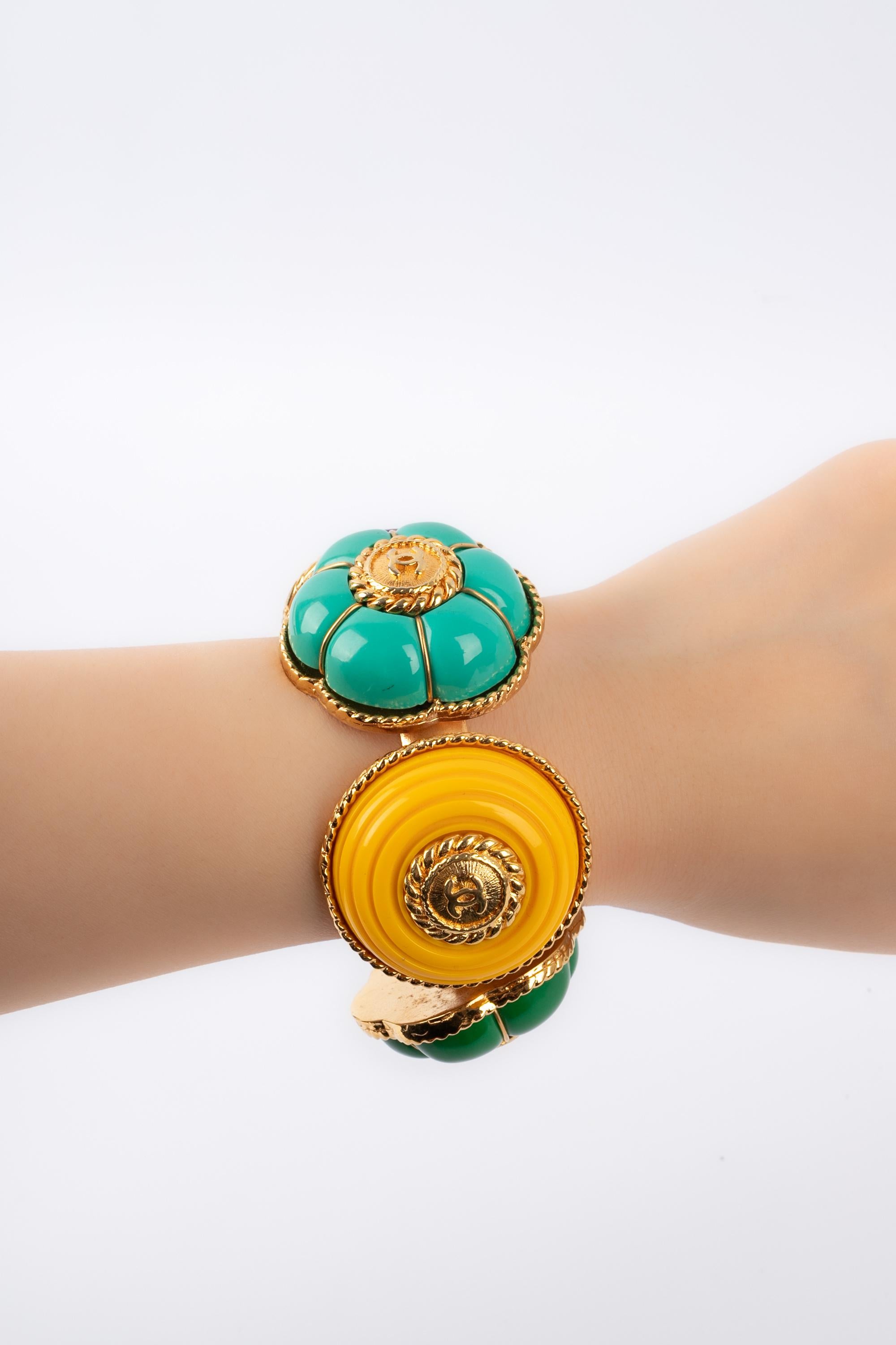 CHANEL - (Made in France) Bracelet rigide en métal doré orné d'éléments en résine colorée.

Condit :
Très bon état.

Dimensions :
Circonférence : 14 cm - Ouverture : 2 cm - Largeur : 4,5 cm

BRAB57