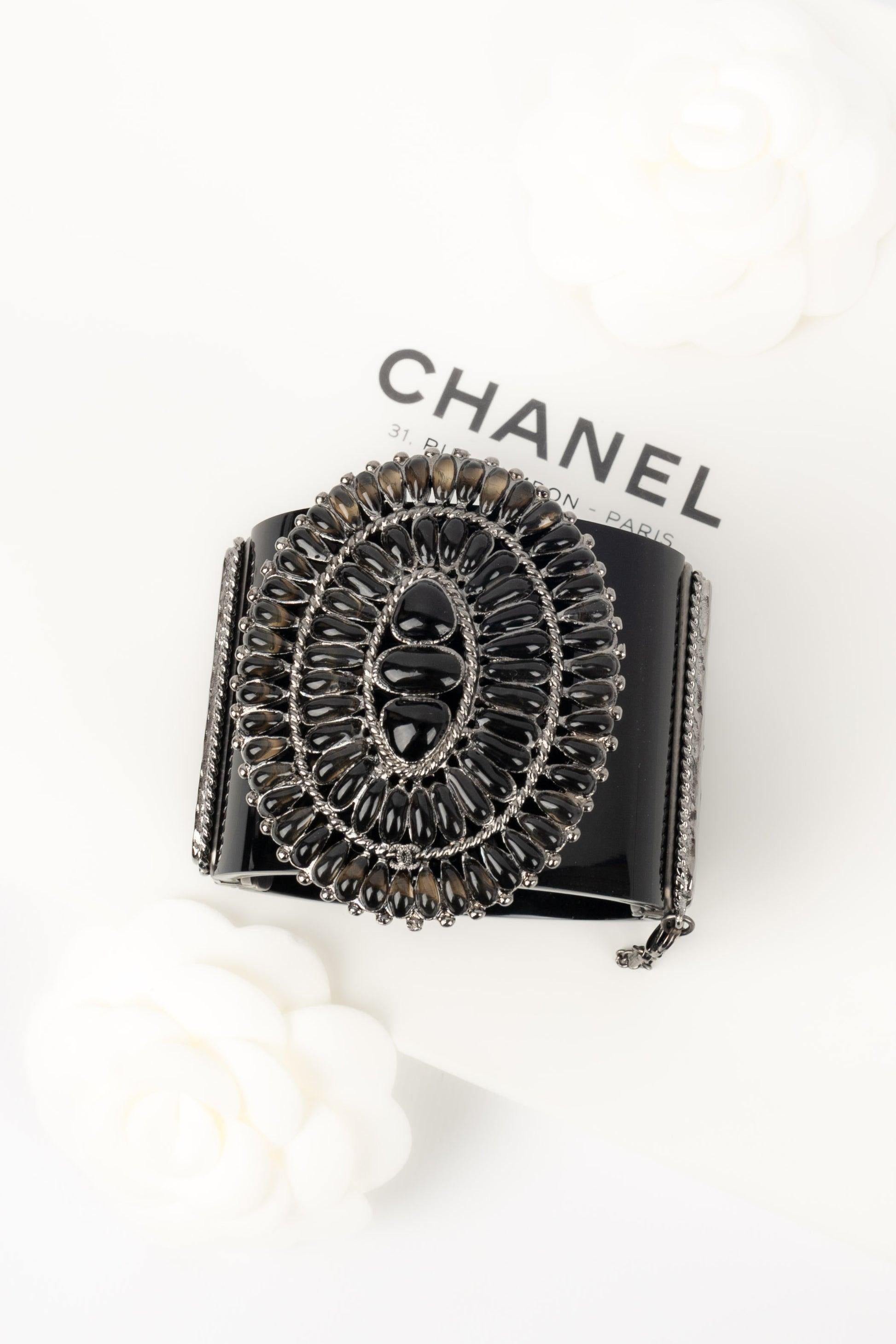 Chanel - (Made in France) Cuff bracelet in black bakelite, silvery metal, and resin.

Additional information:
Condition: Very good condition
Dimensions: Height: 5 cm - Length: 18 cm - Opening: 8 cm

Seller Reference: BRAB114