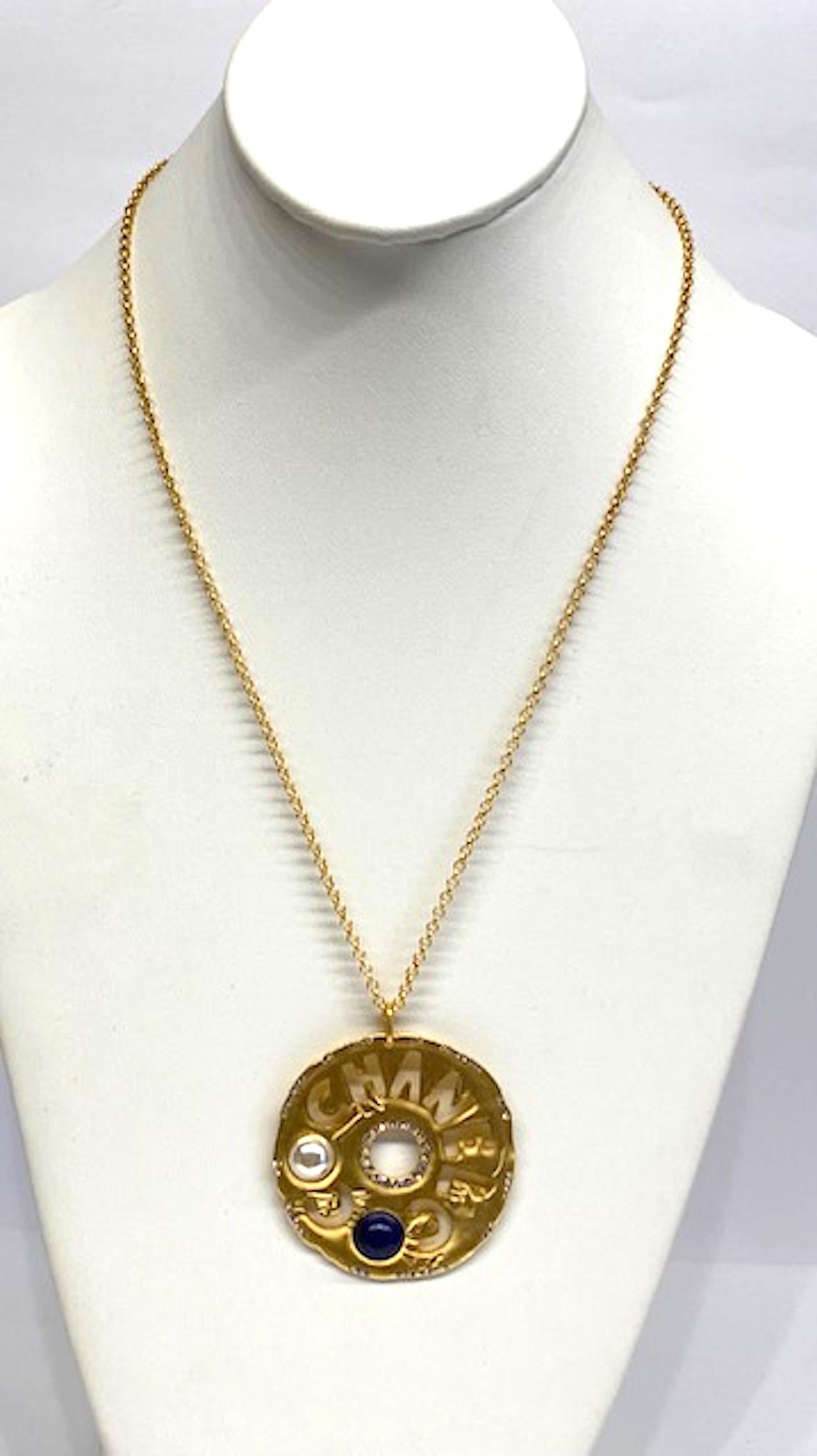 Chanel satin gold cut out pendant necklace from 2019 cruise collection. Pendant and cable link chain are a satin gold tone. The pendant has the words Coco and Chanel cost out. The two Os are set with a faux pearl or a faux glass lapis cabochon. The