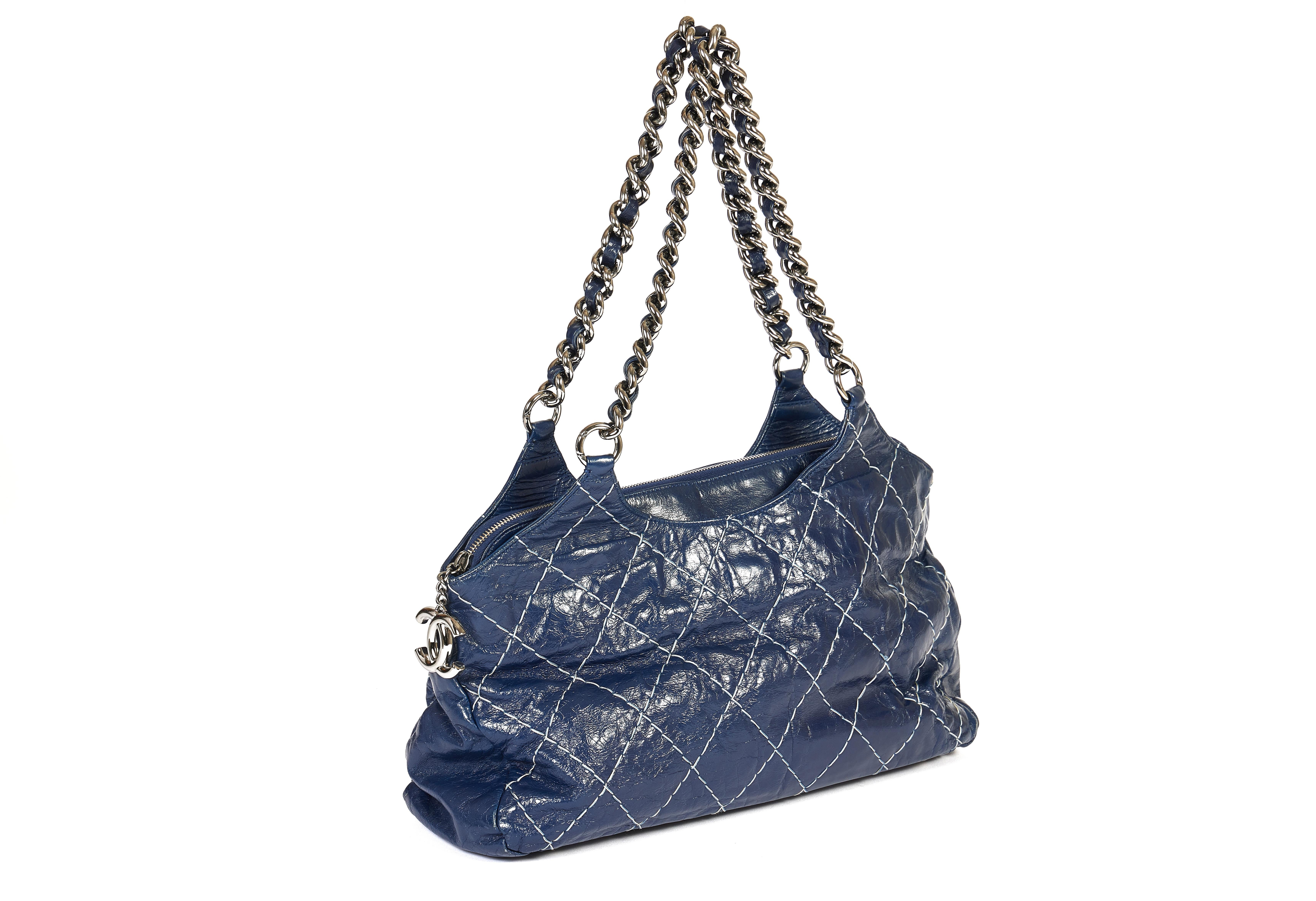 This shoulder bag from Chanel comes in a beautiful dark blue tone. The distressed glazed leather is stitched with a quilted pattern. The two silver shoulder chains match perfectly with the double CC logo from the zipper. The shoulder drop is 11