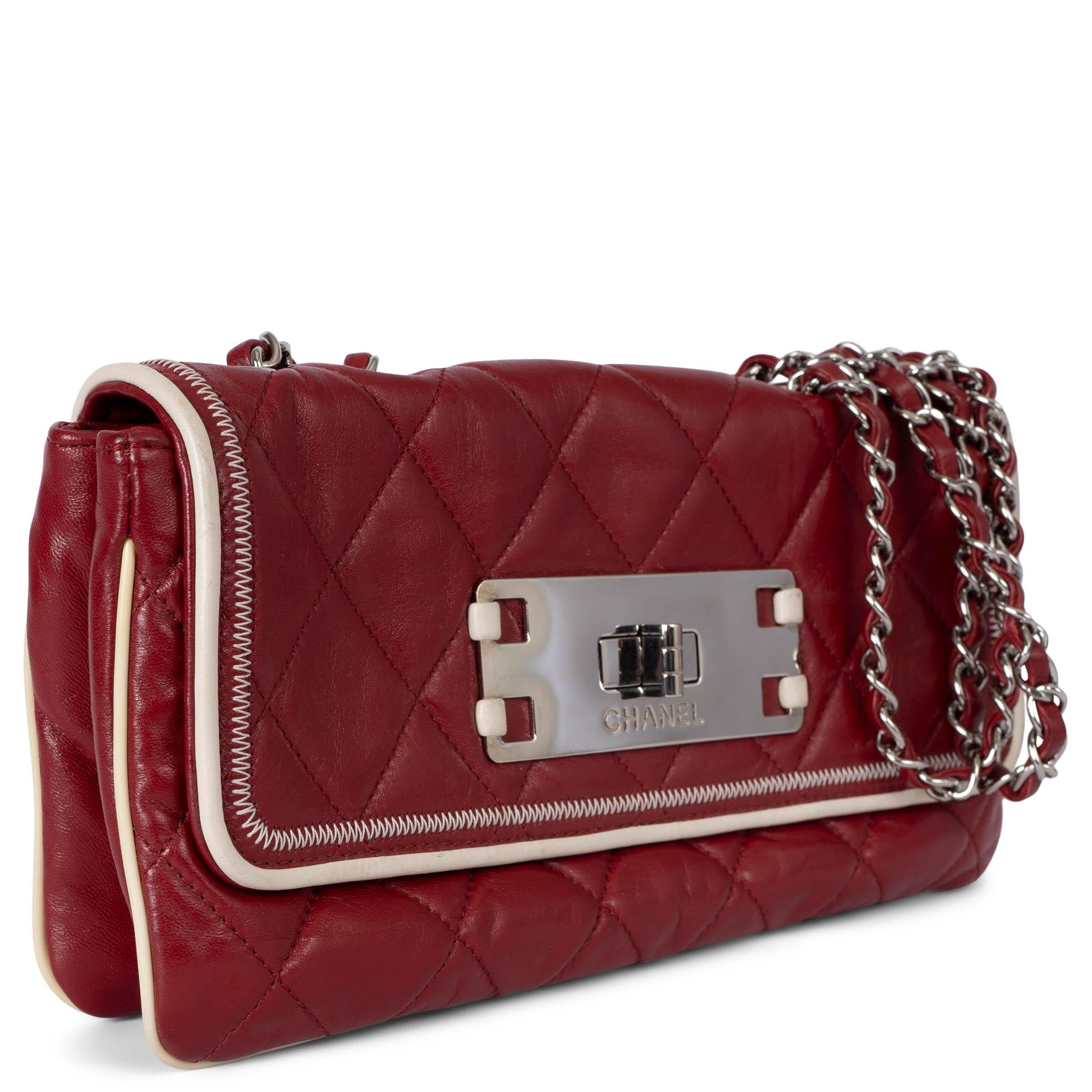 This 100% authentic Chanel Mademoiselle East West flap shoulder bag is crafted from dark red quilted lambskin leather, featuring contrasting white piping and stitching for a striking look. The bag is designed with a silver-tone double chain strap