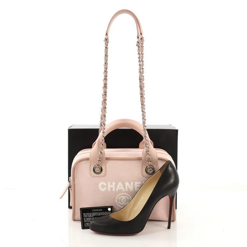 This Chanel Deauville Bowling Bag Canvas Small, crafted in light pink canvas, features dual rolled leather top handles, dual woven-in chain straps with leather pads, Chanel logo and Parisian store address on front, and silver-tone hardware. Its zip