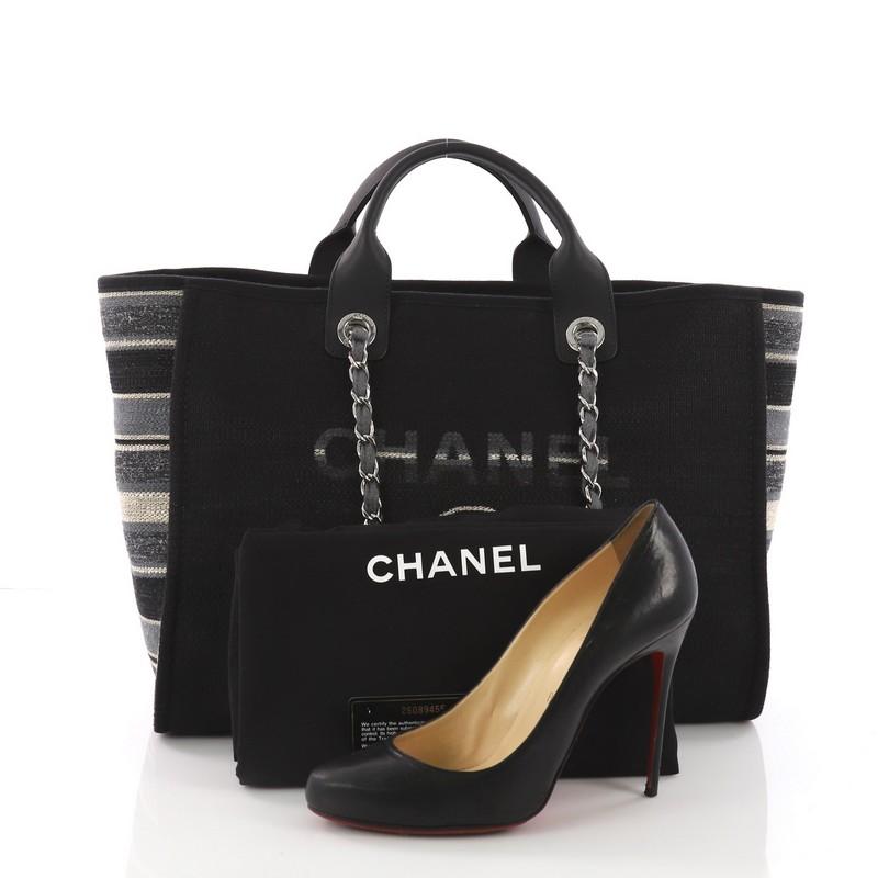 This Chanel Deauville Chain Tote Canvas Large, crafted in black multicolor canvas, features dual flat leather handles, woven-in chain link straps, embroidered CC logo with Chanel's famous Parisian store address, and silver-tone hardware. Its
