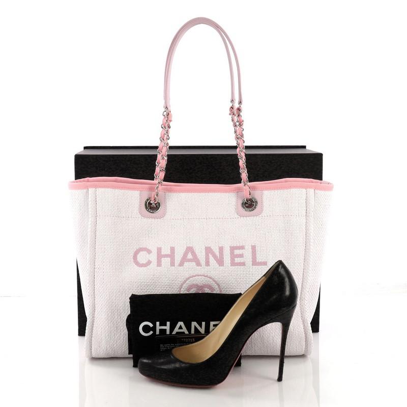 This Chanel Deauville Chain Tote Raffia Small, crafted in light pink raffia, features dual woven-in canvas chain straps, printed CC logo, and silver-tone hardware. Its magnetic snap closure opens to a pink fabric interior with slip and zip pockets.