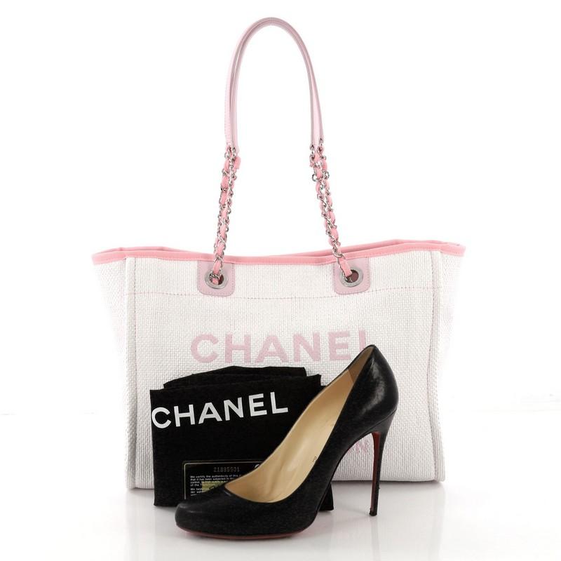 This Chanel Deauville Chain Tote Raffia Small, crafted in white and pink raffia, features dual woven-in canvas chain straps, printed CC logo, and silver-tone hardware. Its magnetic snap closure opens to a pink fabric interior with slip and zip