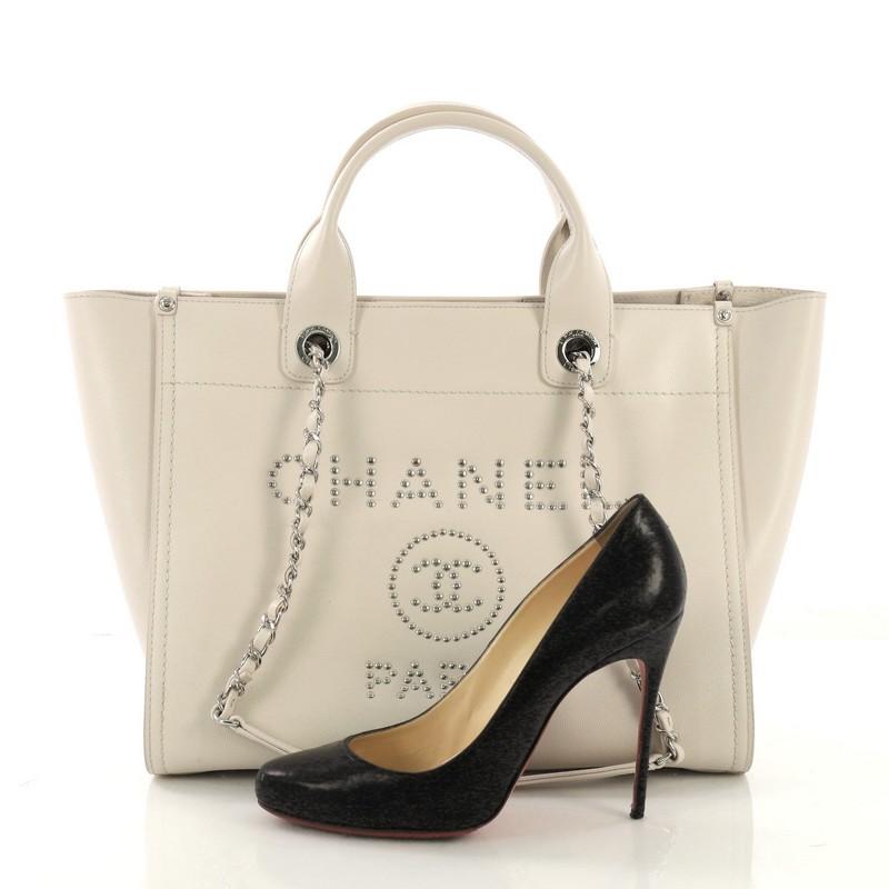 This Chanel Deauville Chain Tote Studded Caviar Small, crafted in off white caviar leather, features dual woven-in leather chain straps, dual top handles, studded logo at the front, and silver-tone hardware. Its magnetic snap closure opens to a tan