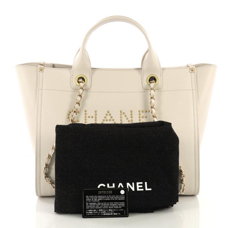This Chanel Deauville Chain Tote Studded Caviar Small, crafted in nude studded caviar leather, features dual woven-in leather chain straps, dual top handles, studded logo at the front, and matte gold-tone hardware. Its magnetic snap closure opens to